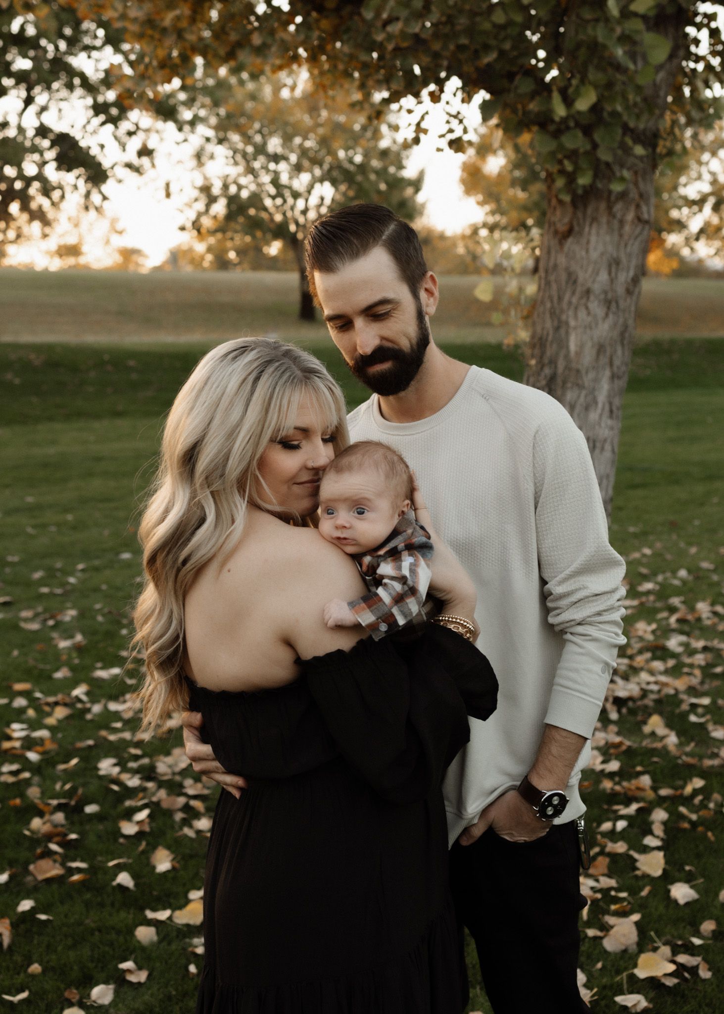 Family portrait in autumn setting with baby under tree with fallen leaves.