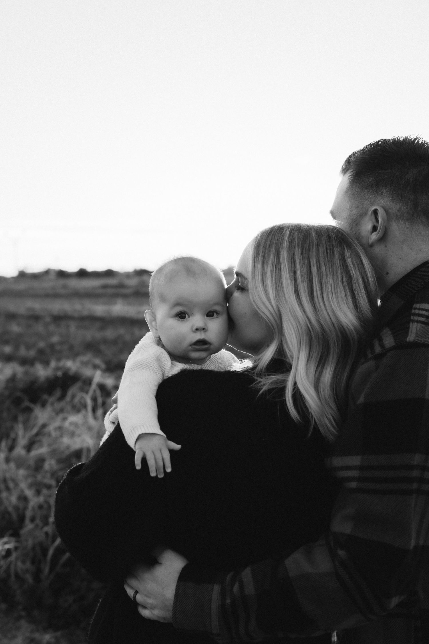A loving outdoor family portrait showing parents holding their baby at sunset.