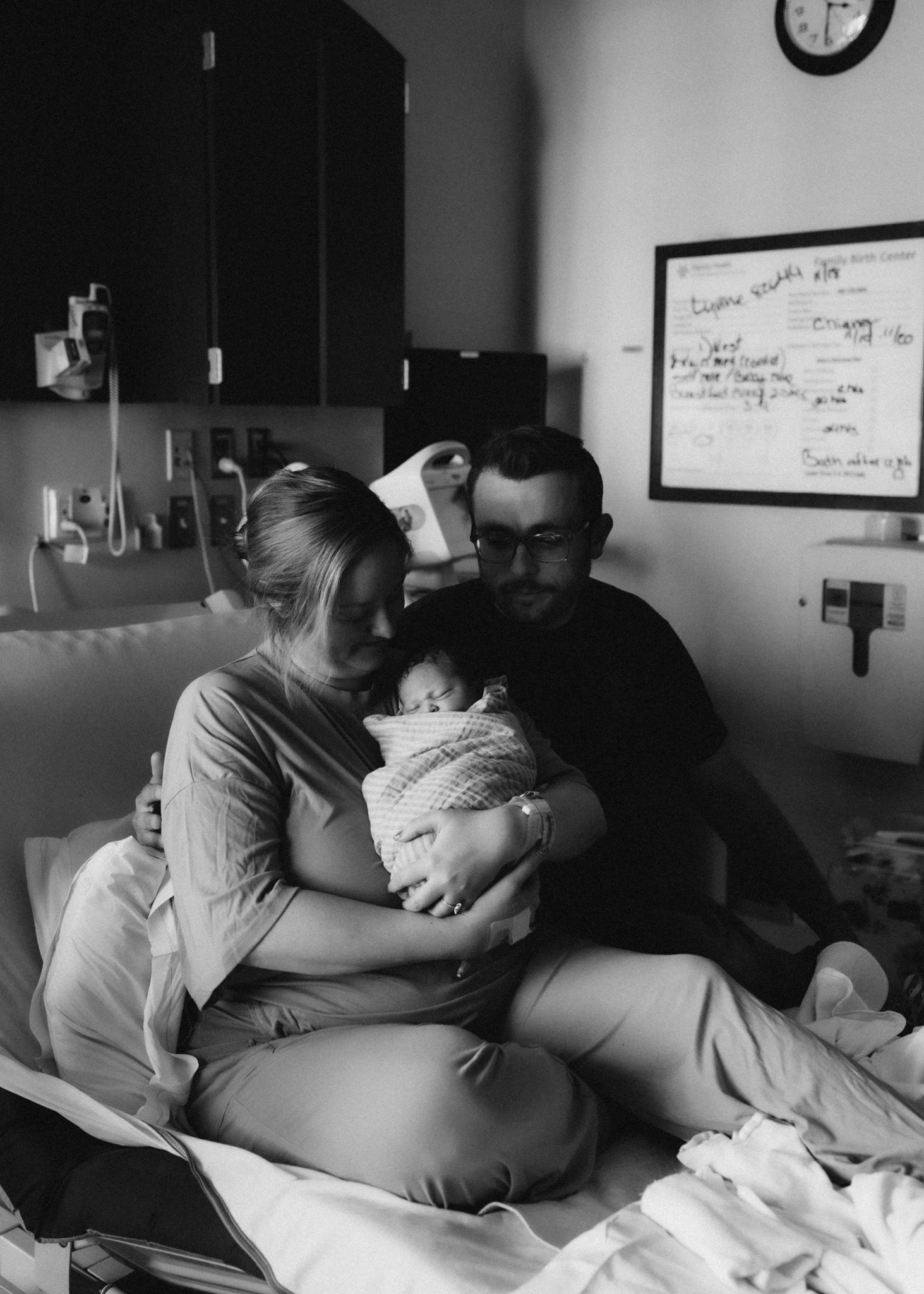 Black and white photo capturing a tender family moment with a newborn in a hospital setting.