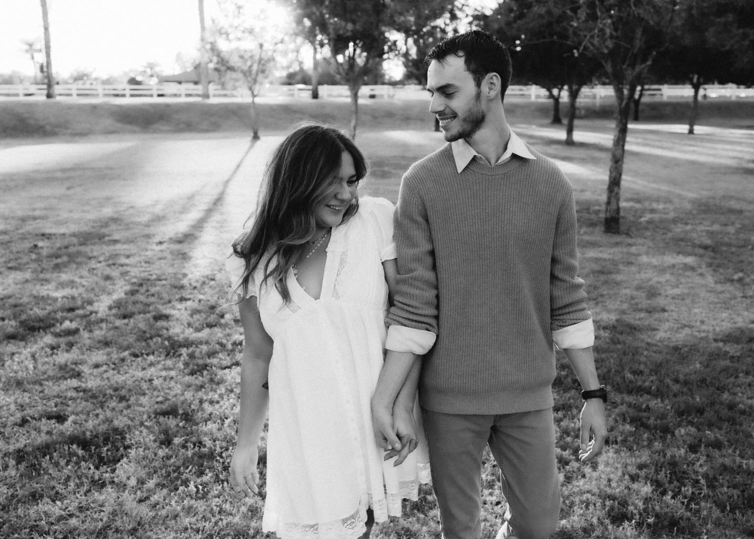 A black and white portrait of a couple sharing a joyful moment in an outdoor park setting.