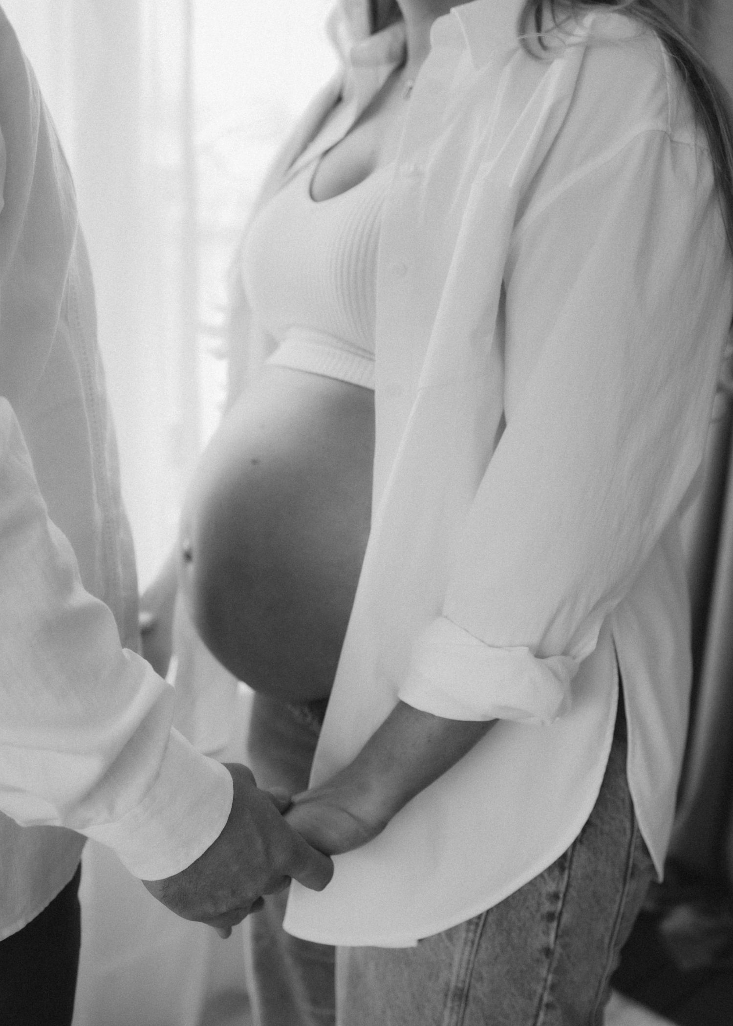 Black and white photo showing a pregnant woman in a white button-up shirt holding hands with someone next to her.