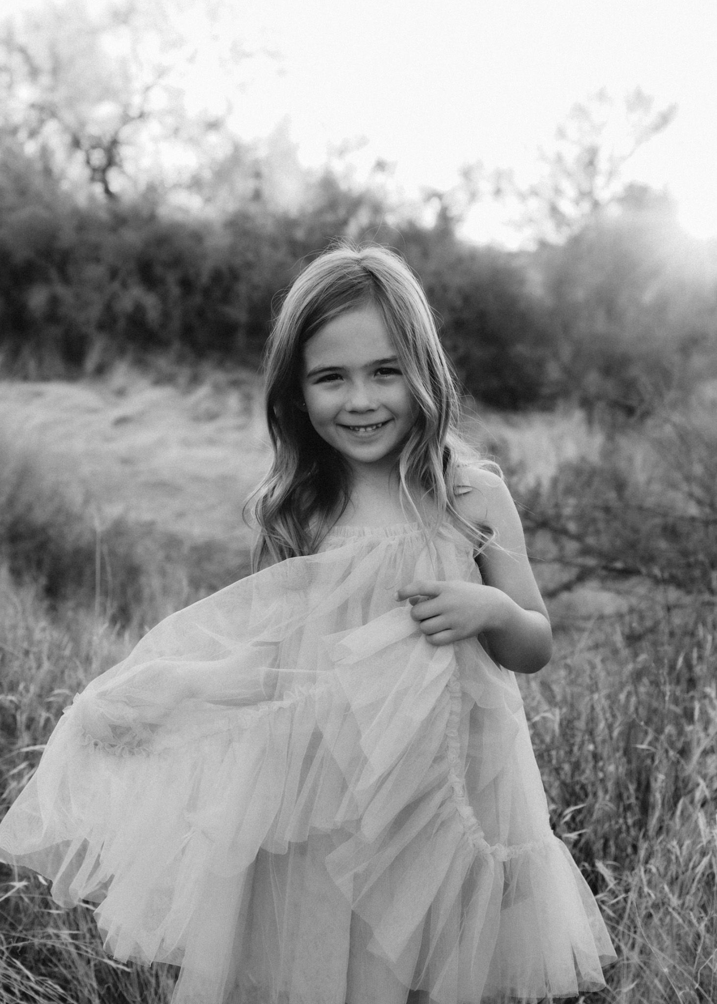 Black and white portrait of young person in flowing tulle dress outdoors.