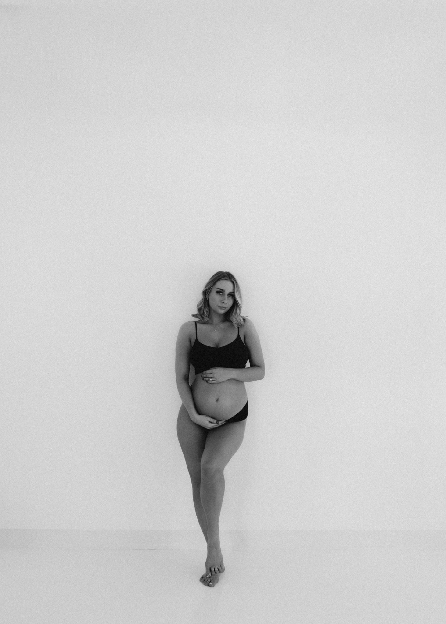 Minimalist black and white maternity portrait against plain wall.