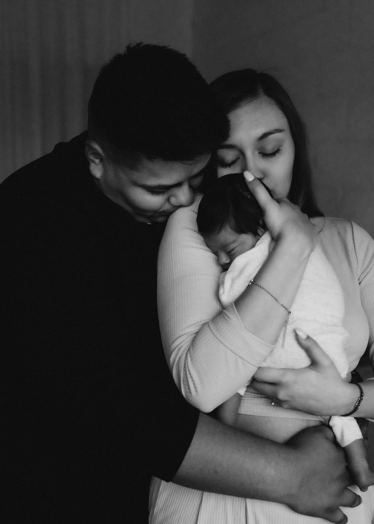 Intimate black and white family portrait with sleeping newborn in white outfit.