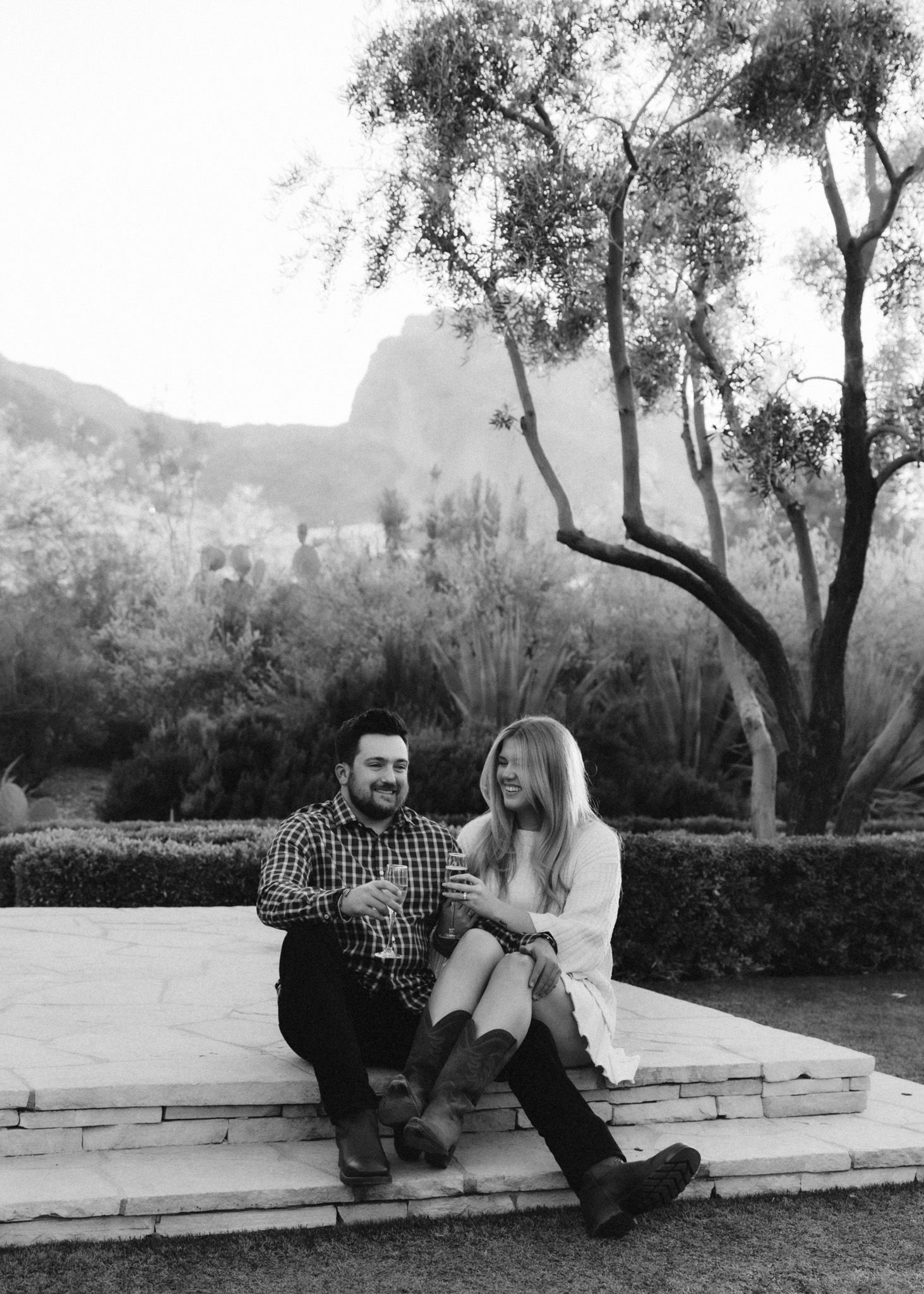 Black and white portrait of couple sitting on stone steps with mountain backdrop.