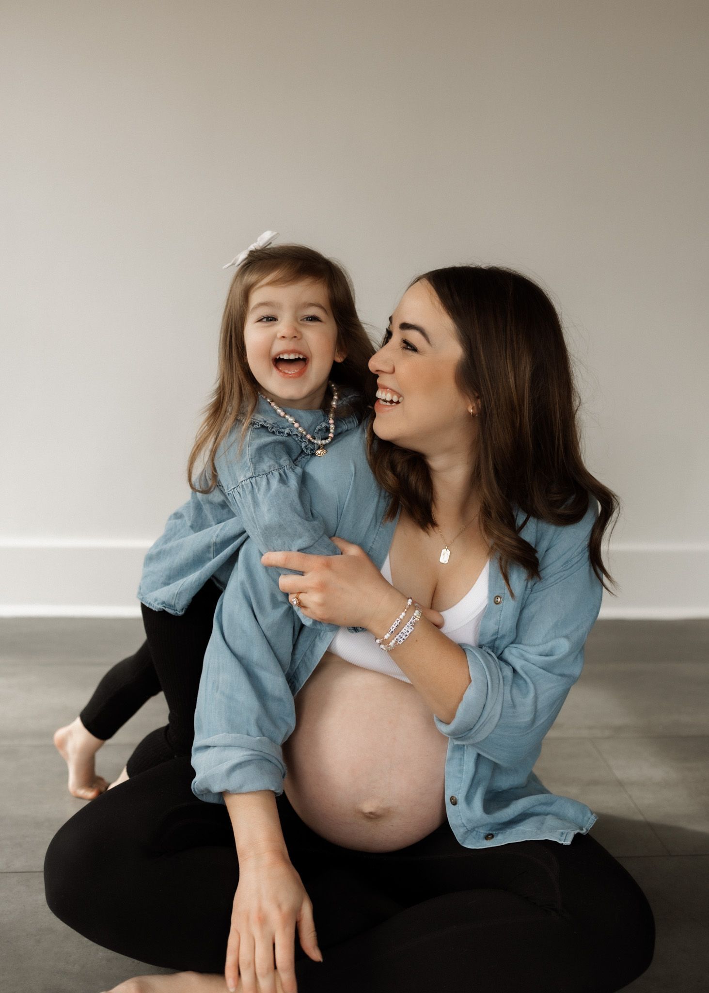 Maternity moment with denim-clad mom and daughter sharing joyful laughter.