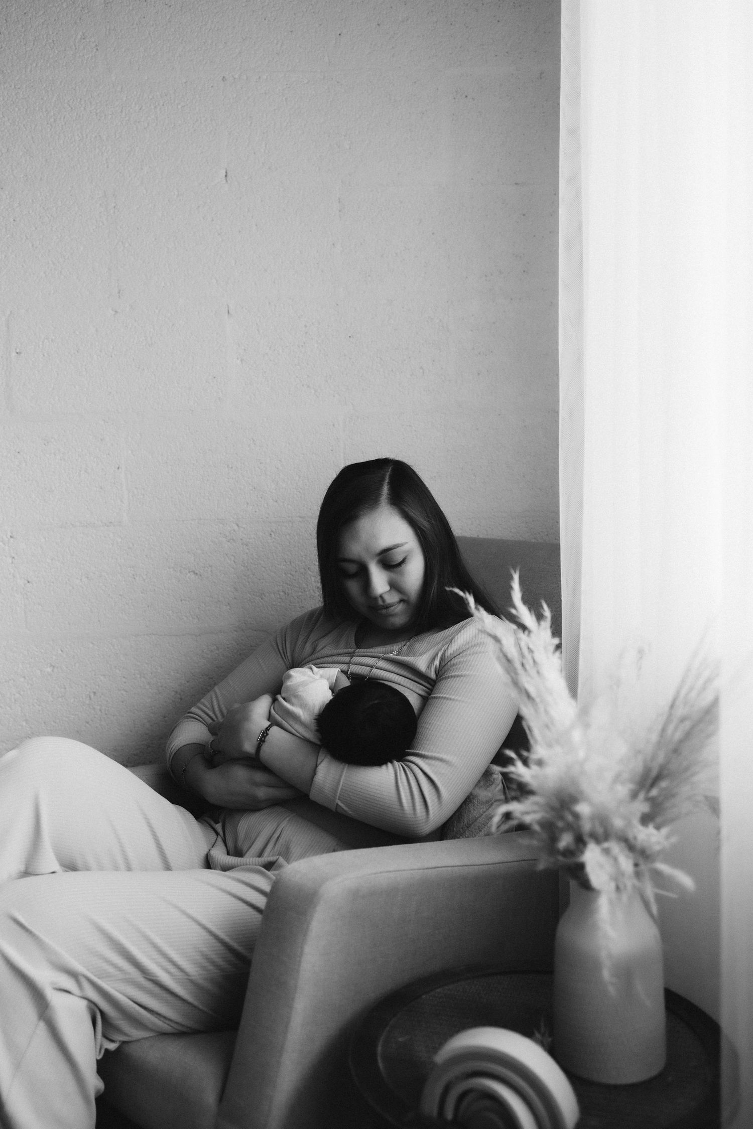 Intimate black and white photo of tender nursing moment in a quiet corner with vase decoration.