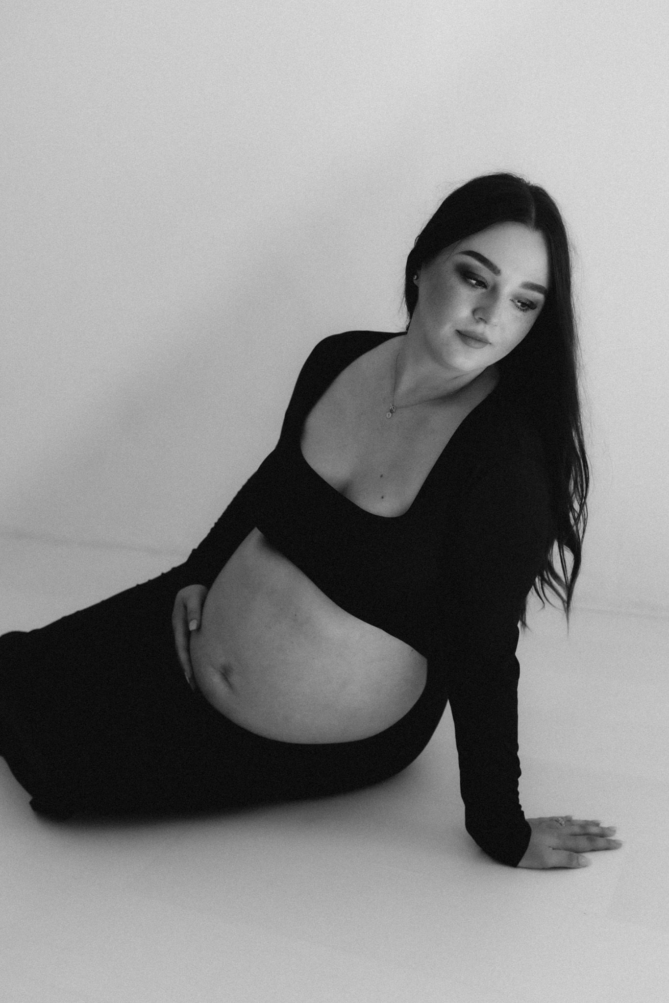 Artistic maternity photo of an expectant mother in black attire against a white backdrop.