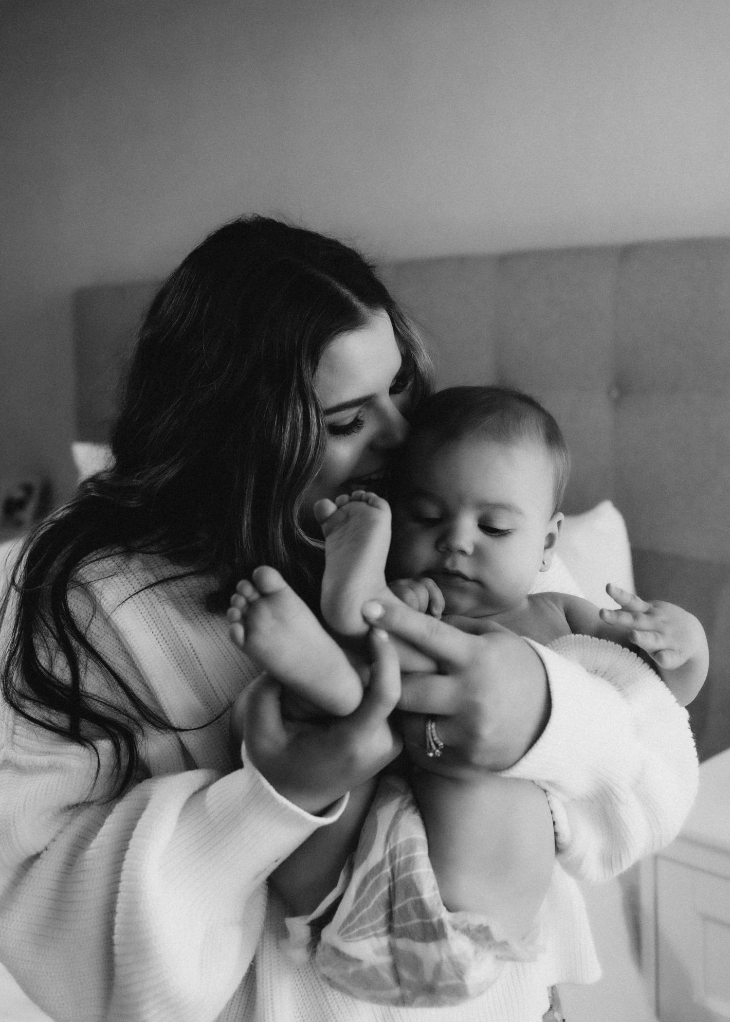 Tender black and white moment between a parent and baby on a bed.