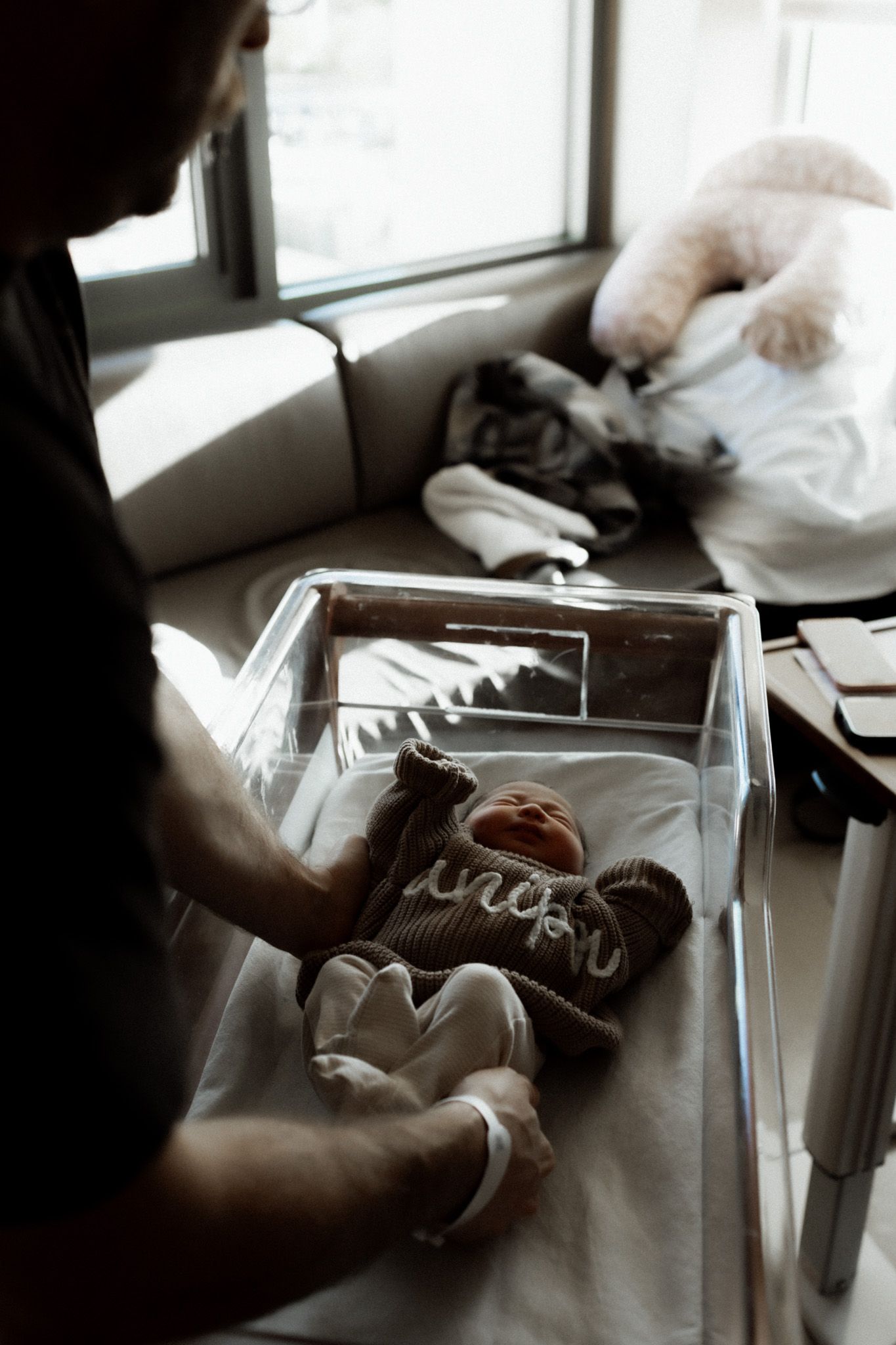 Baby shoes and clothing being arranged in a clear box near a window with soft natural lighting.