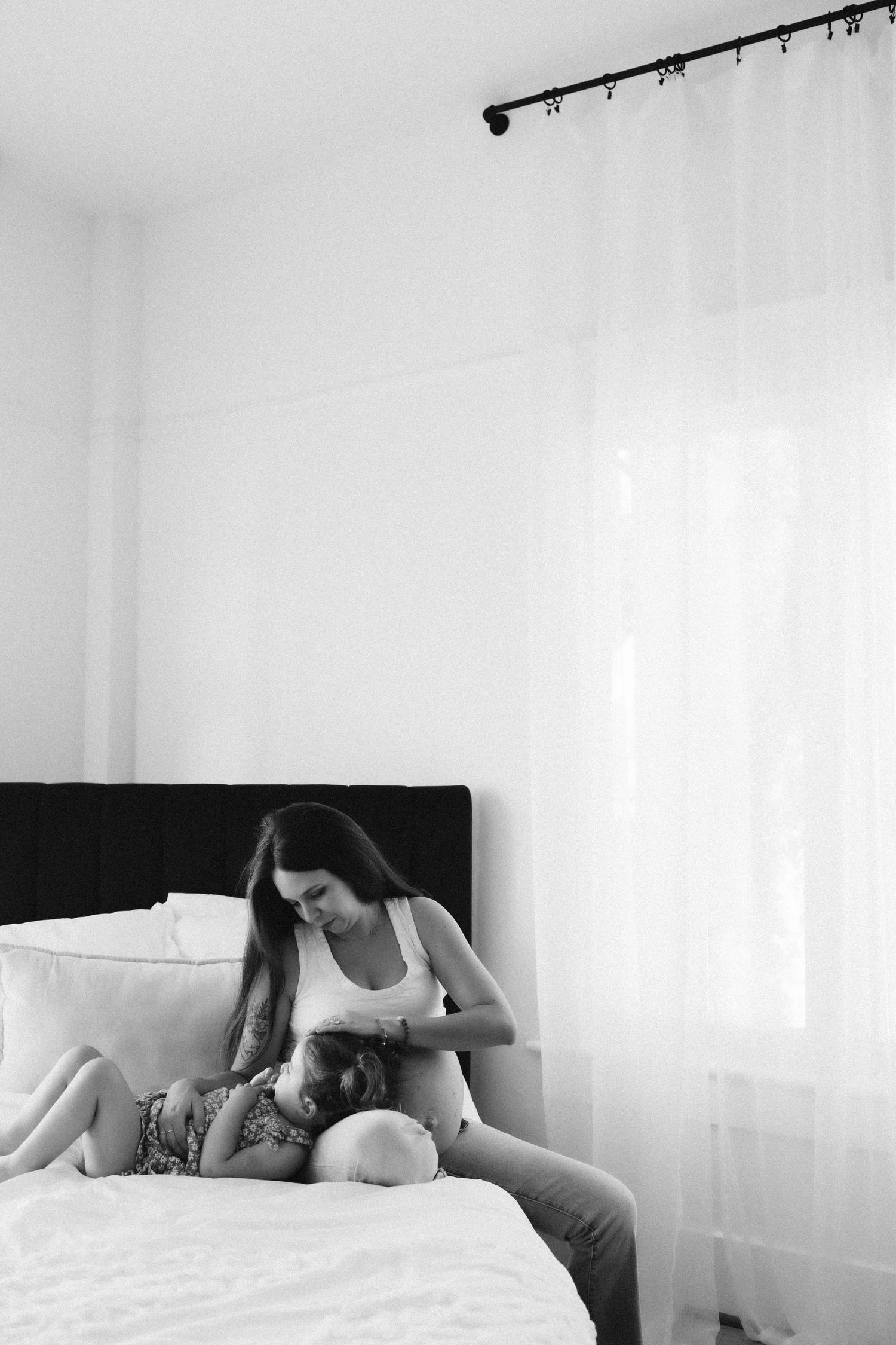 Black and white photo showing tender moment between parent and child on white bed.