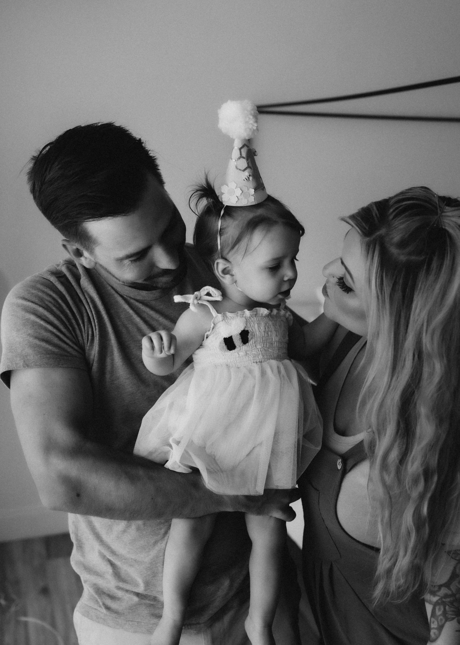 Family portrait with baby wearing white dress and party hat.