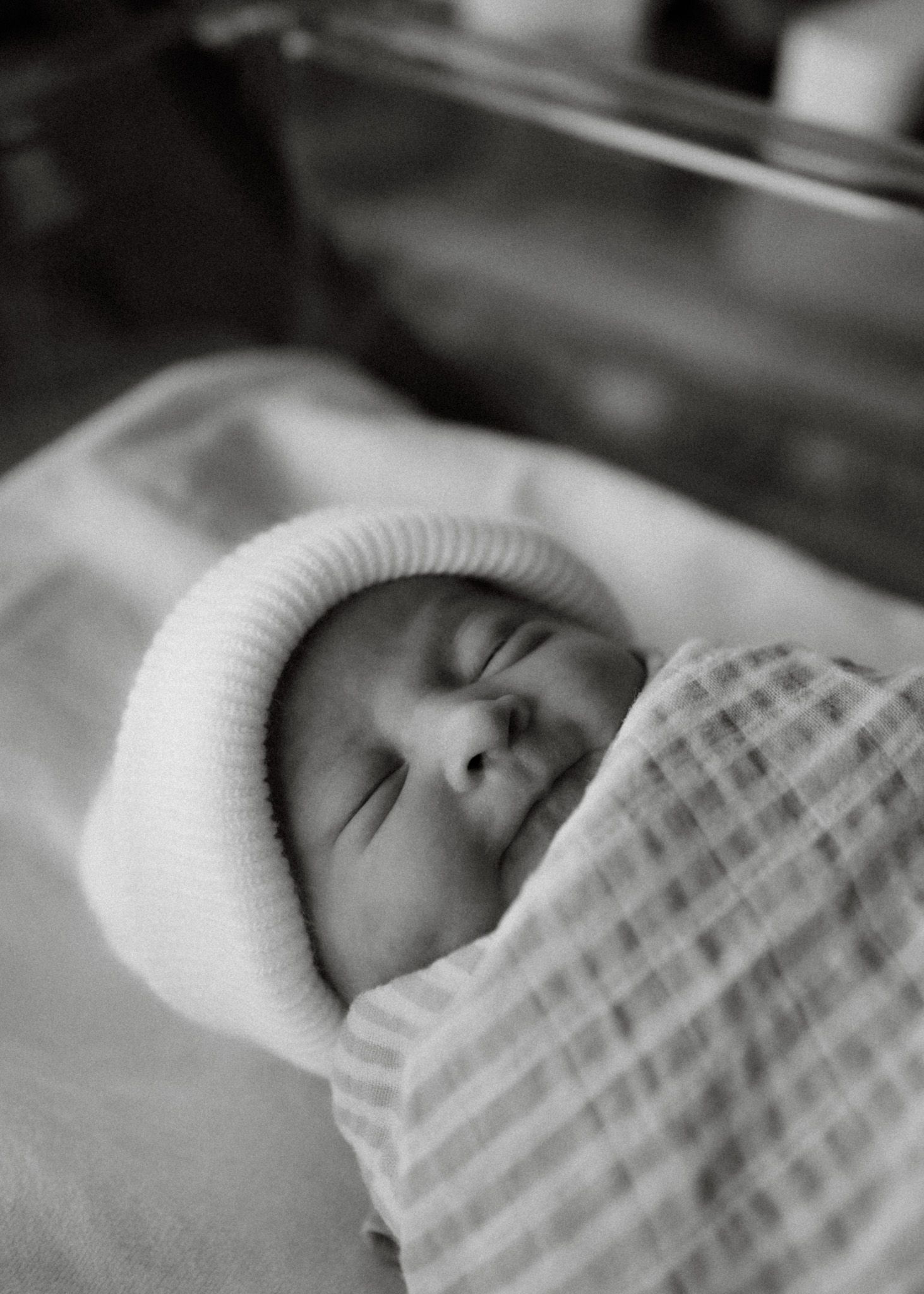 A sleeping newborn swaddled in a blanket wearing a white knit hat.