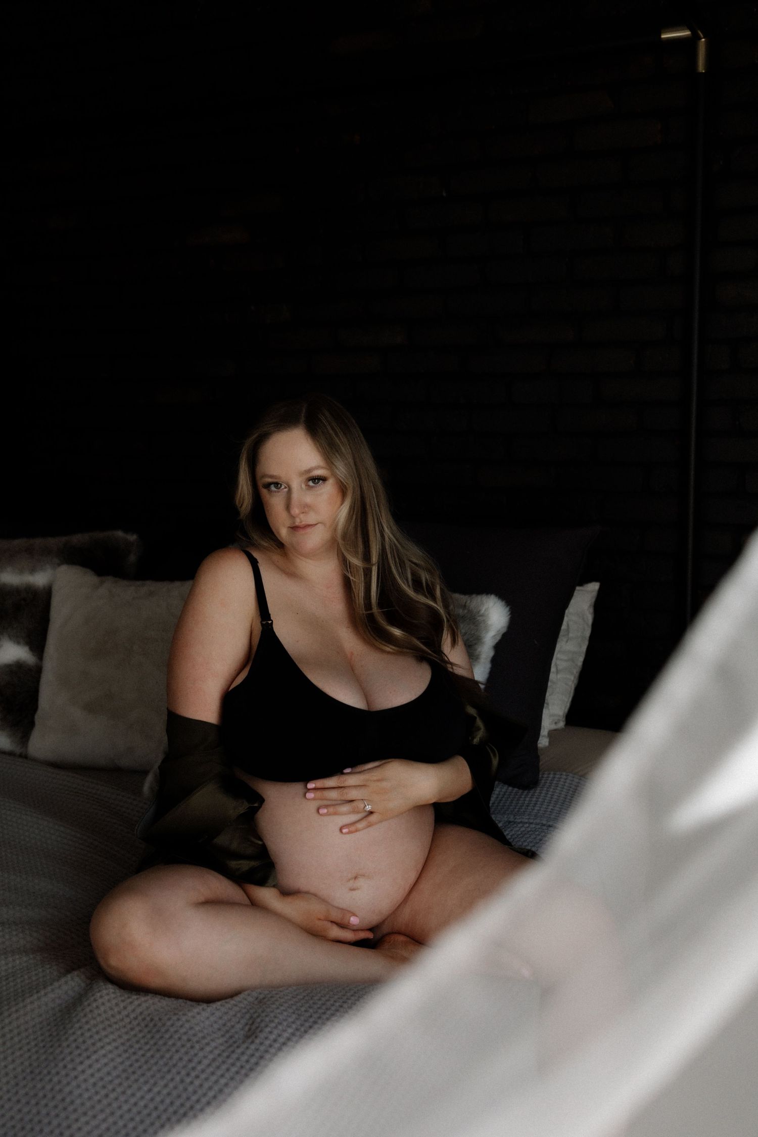 Artistic maternity boudoir photo on gray bedding with natural window light.