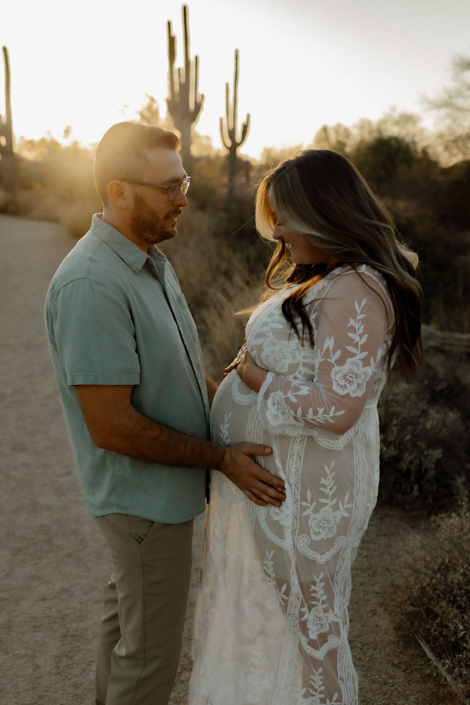 A couple shares an intimate moment during sunset in the desert, surrounded by towering saguaro cacti.