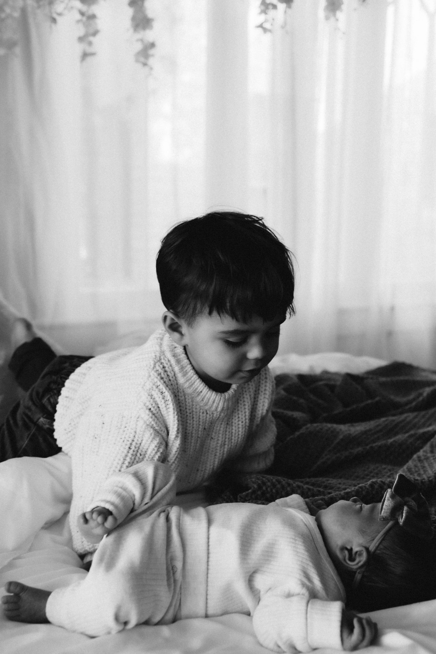 Black and white photo of siblings sharing a tender moment on bed.