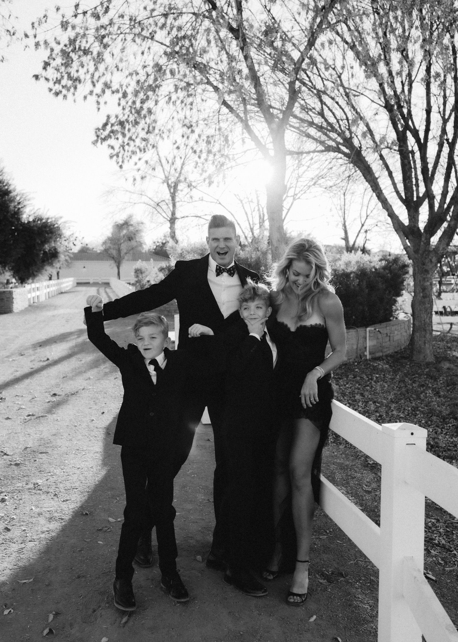 Family portrait on a tree-lined path with children in formal attire.