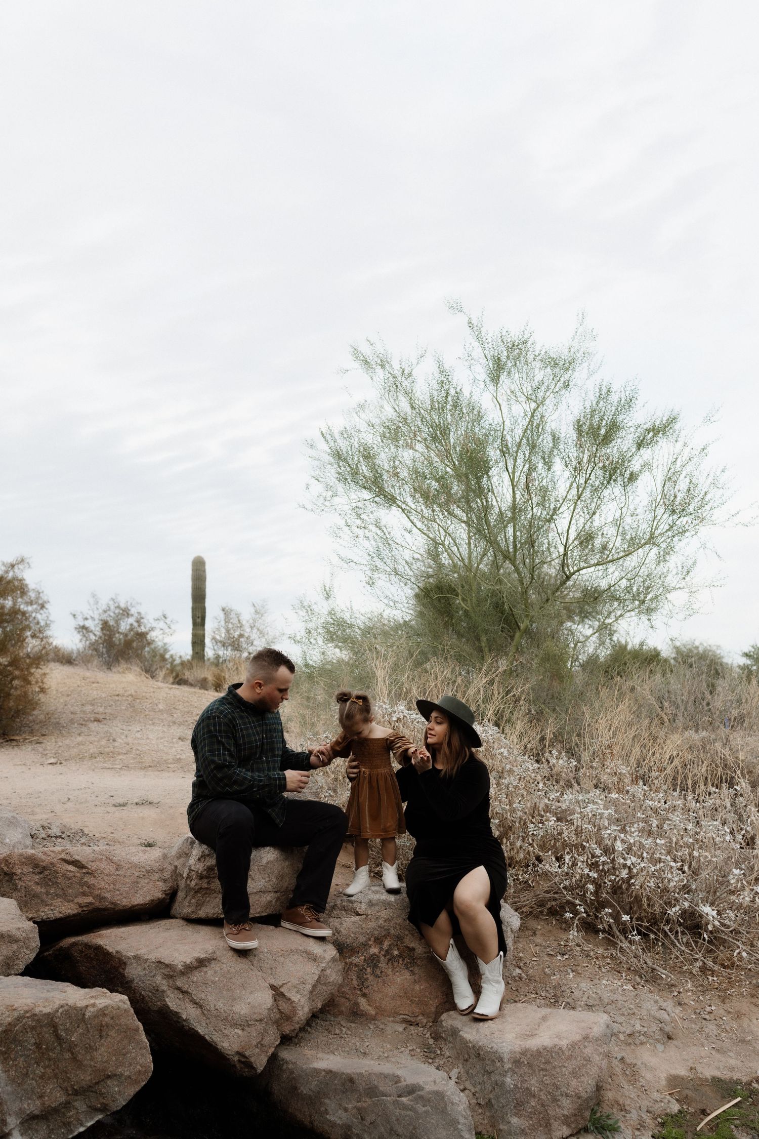 Family sitting together on desert rocks surrounded by cacti and desert vegetation.