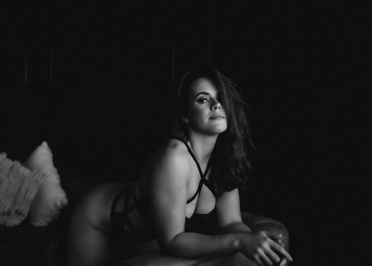 Dramatic black and white portrait in intimate lighting on textured bedding.