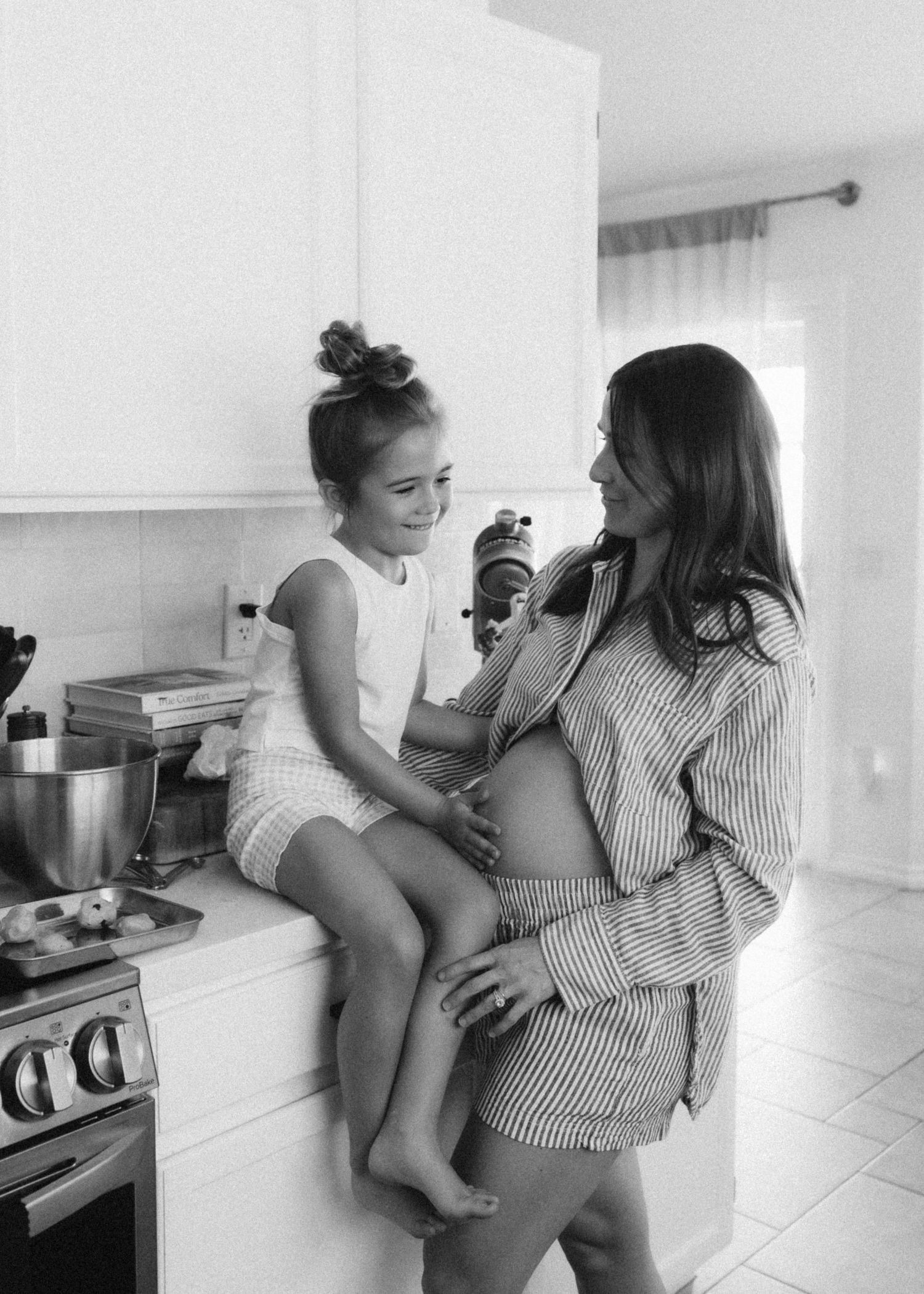 Candid black and white photos show tender moment of mother and toddler playing in a bright kitchen interior.