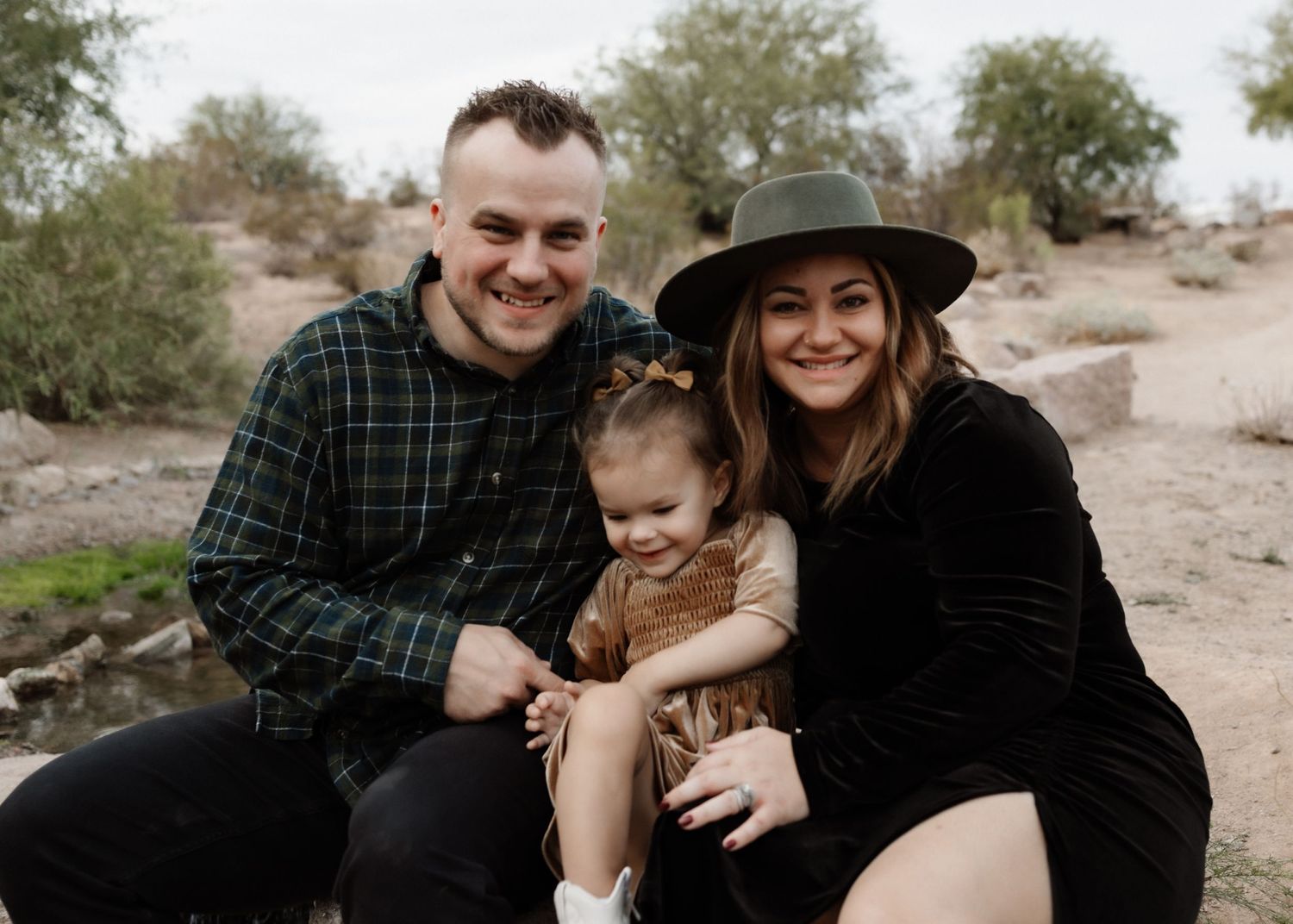 Family wearing casual attire sits together on rocks in desert landscape.