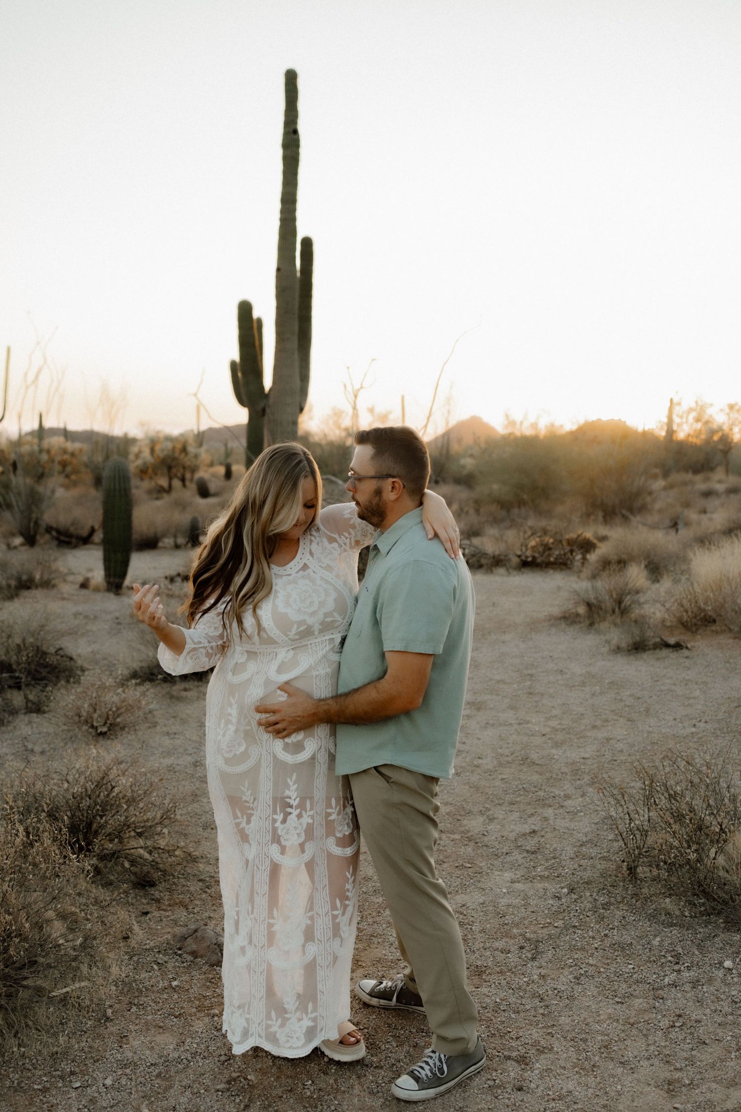 A couple embraces on a desert trail with a majestic saguaro cactus silhouetted against the sunset.