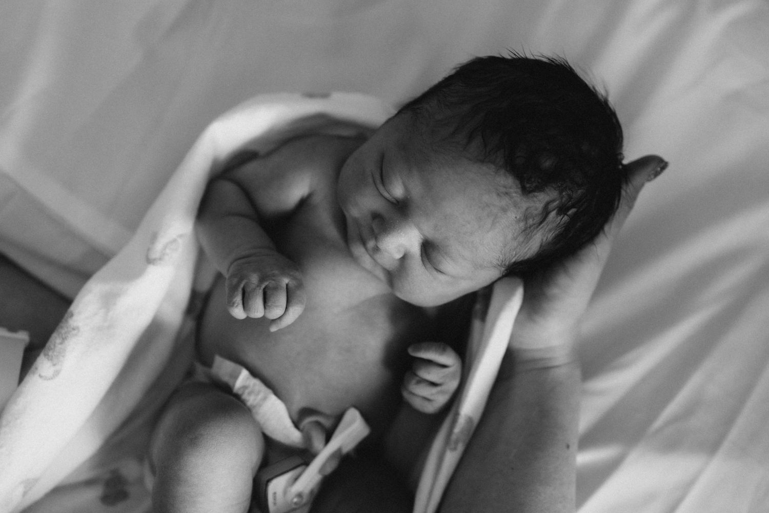 Tender black and white photo of skin-to-skin contact with a newborn baby.