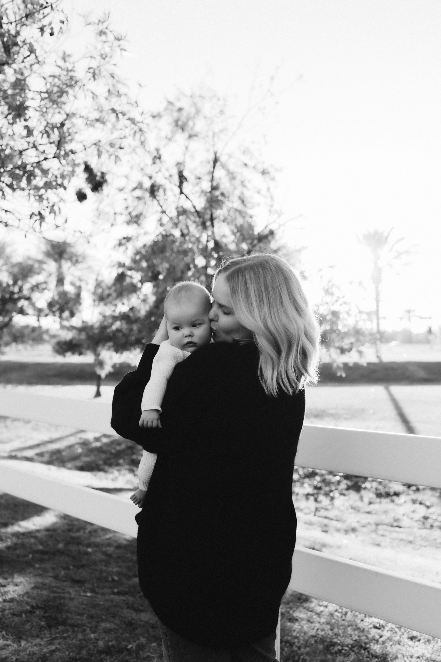Tender moment between parent and baby against rustic fence background.
