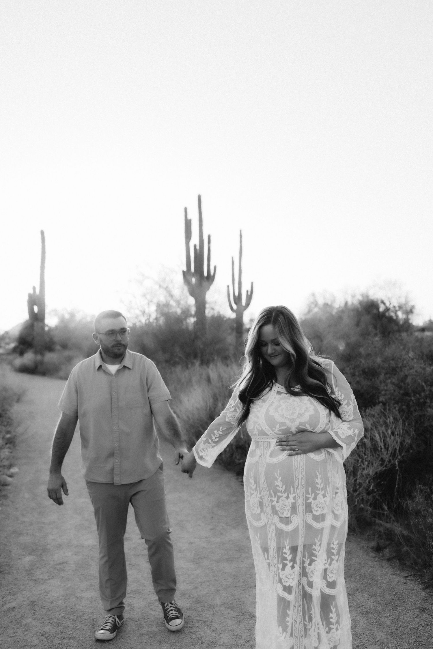Black and white desert photo of couple walking hand in hand with saguaro cacti in background.
