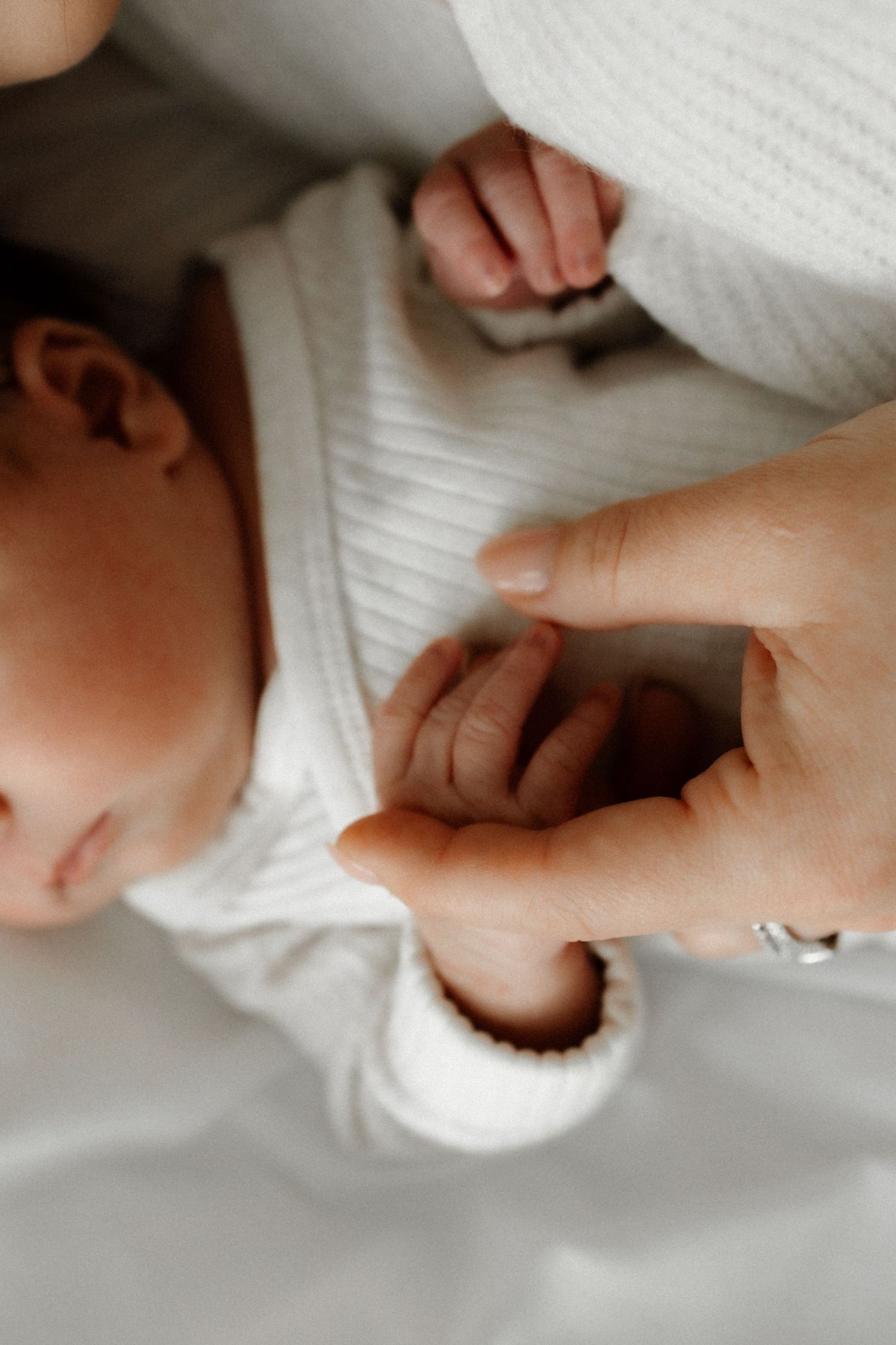 Close-up view of tiny baby hands being held against white knitted fabric.