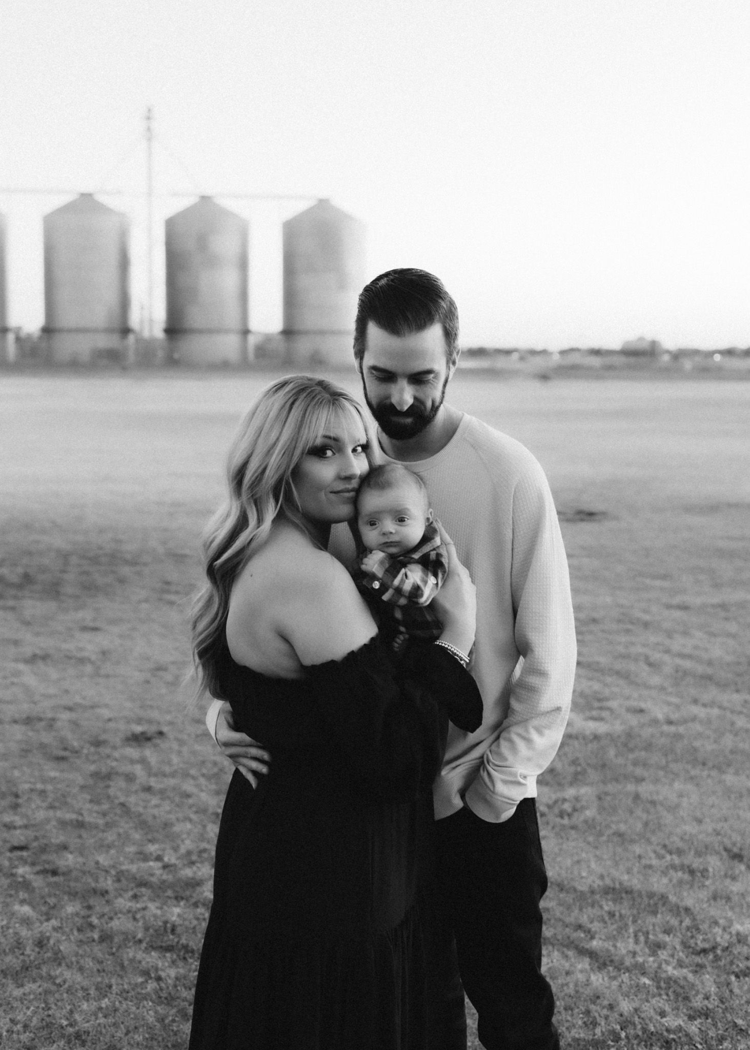 Family portrait with baby in monochrome against backdrop of rural grain silos.