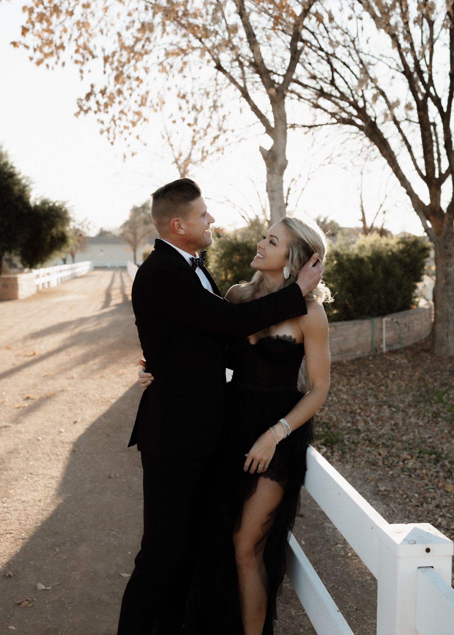 Romantic couple in formal wear embrace on a path with autumn trees in the background.