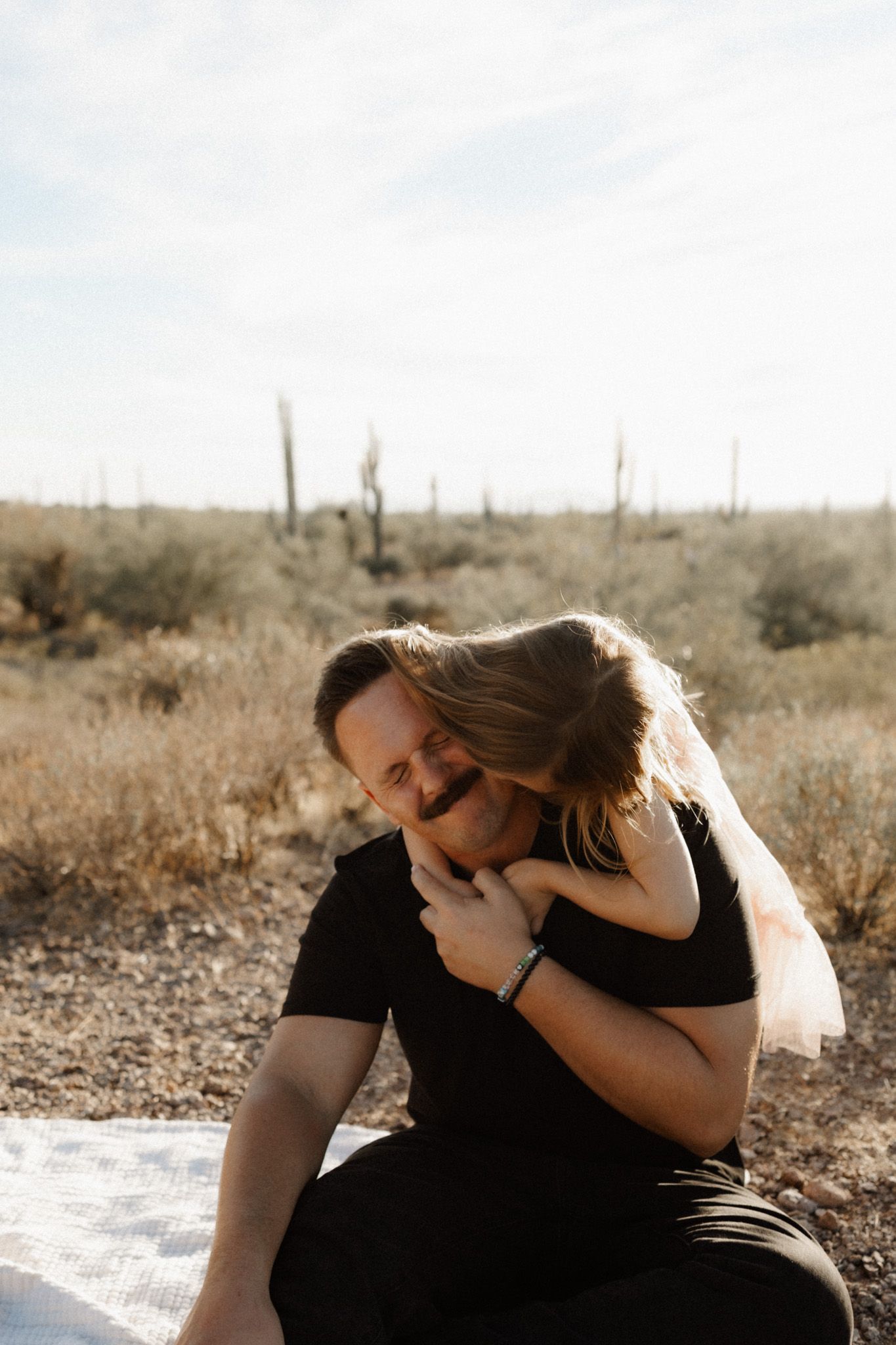 Intimate moment captured in desert setting with saguaro cacti in background.