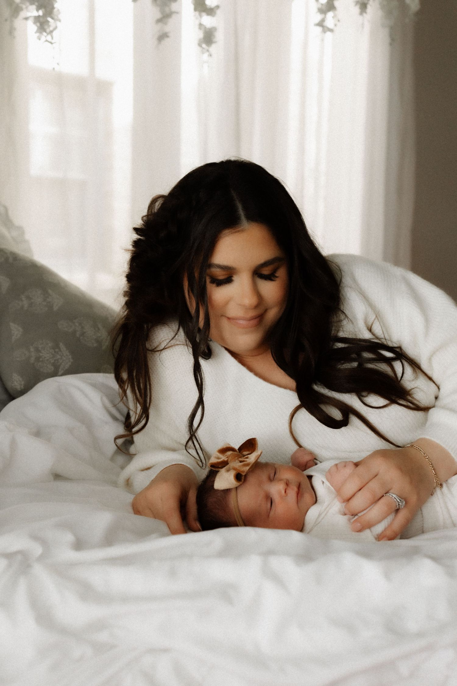 A sweet moment between a caregiver and baby on white bedding in natural window light.
