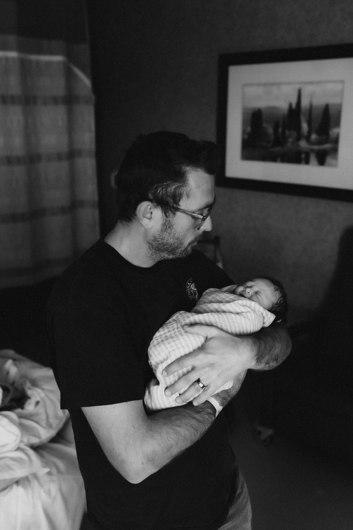 Parent holding sleeping newborn baby in hospital room.