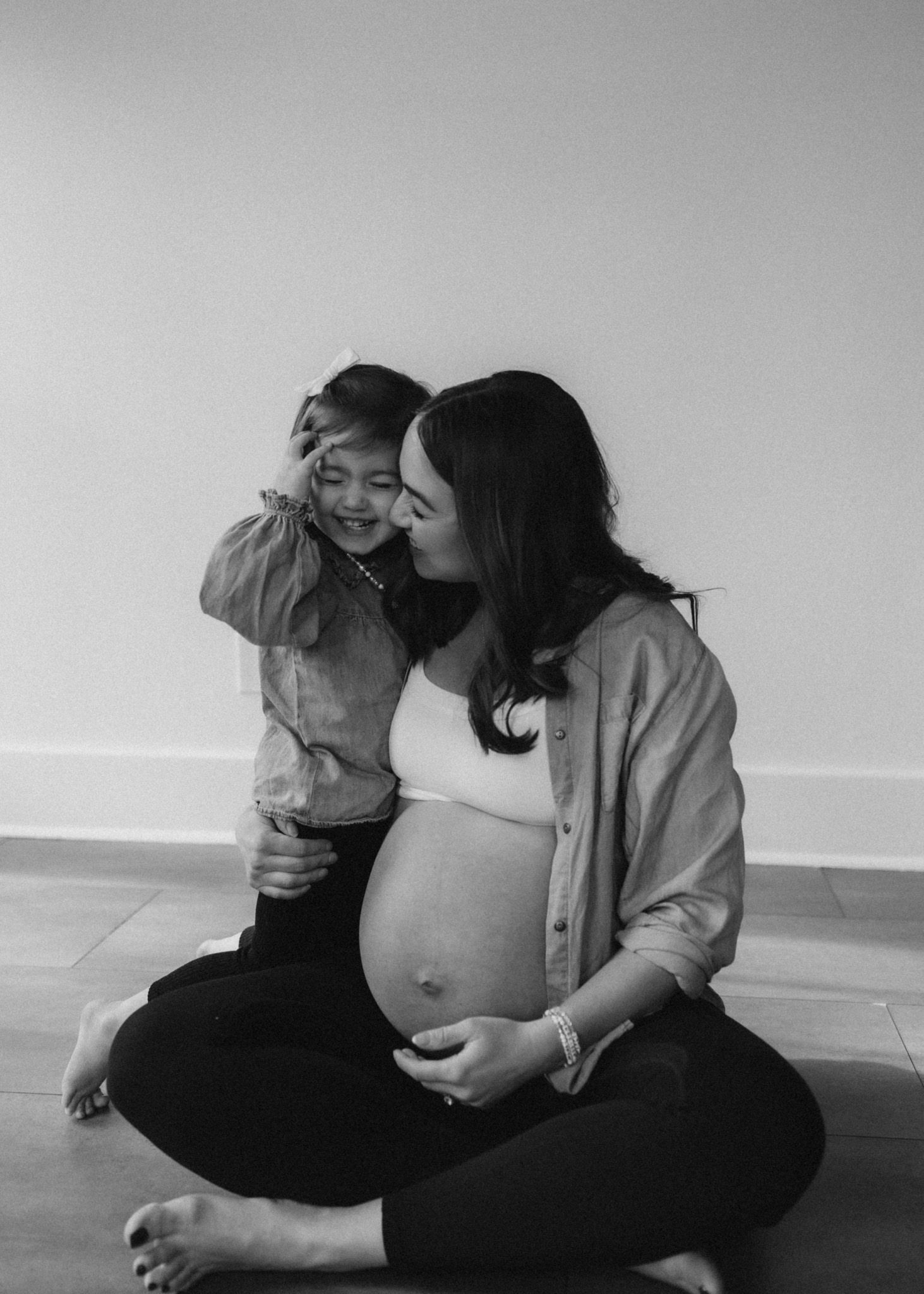 Black and white photo of pregnant parent sharing tender moment with toddler.