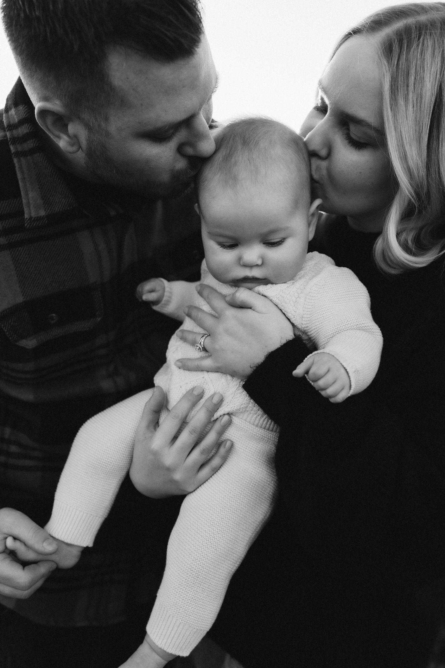 A tender family moment captured in black and white as parents kiss their baby.