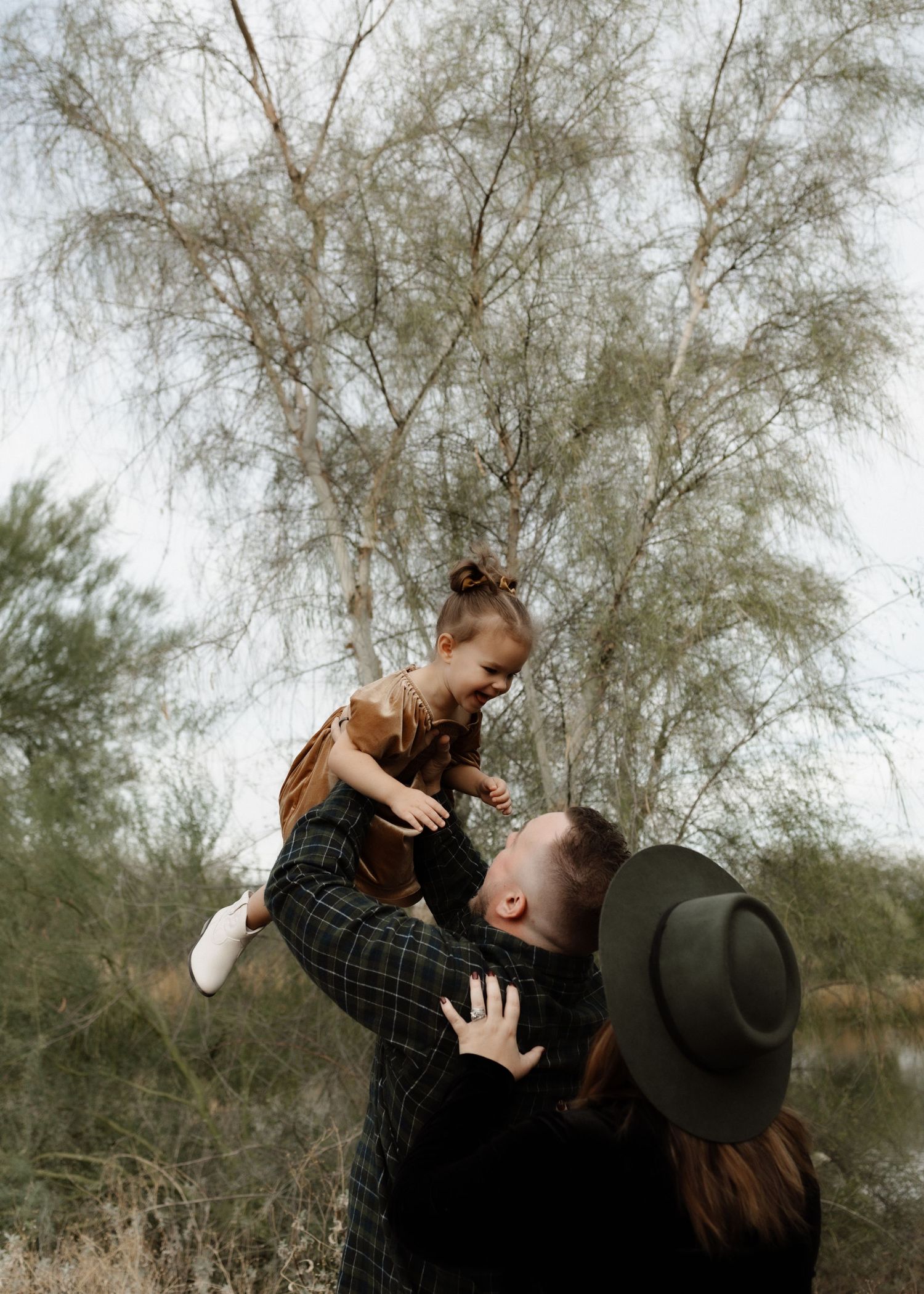 A playful family moment captured under tall trees with natural lighting.