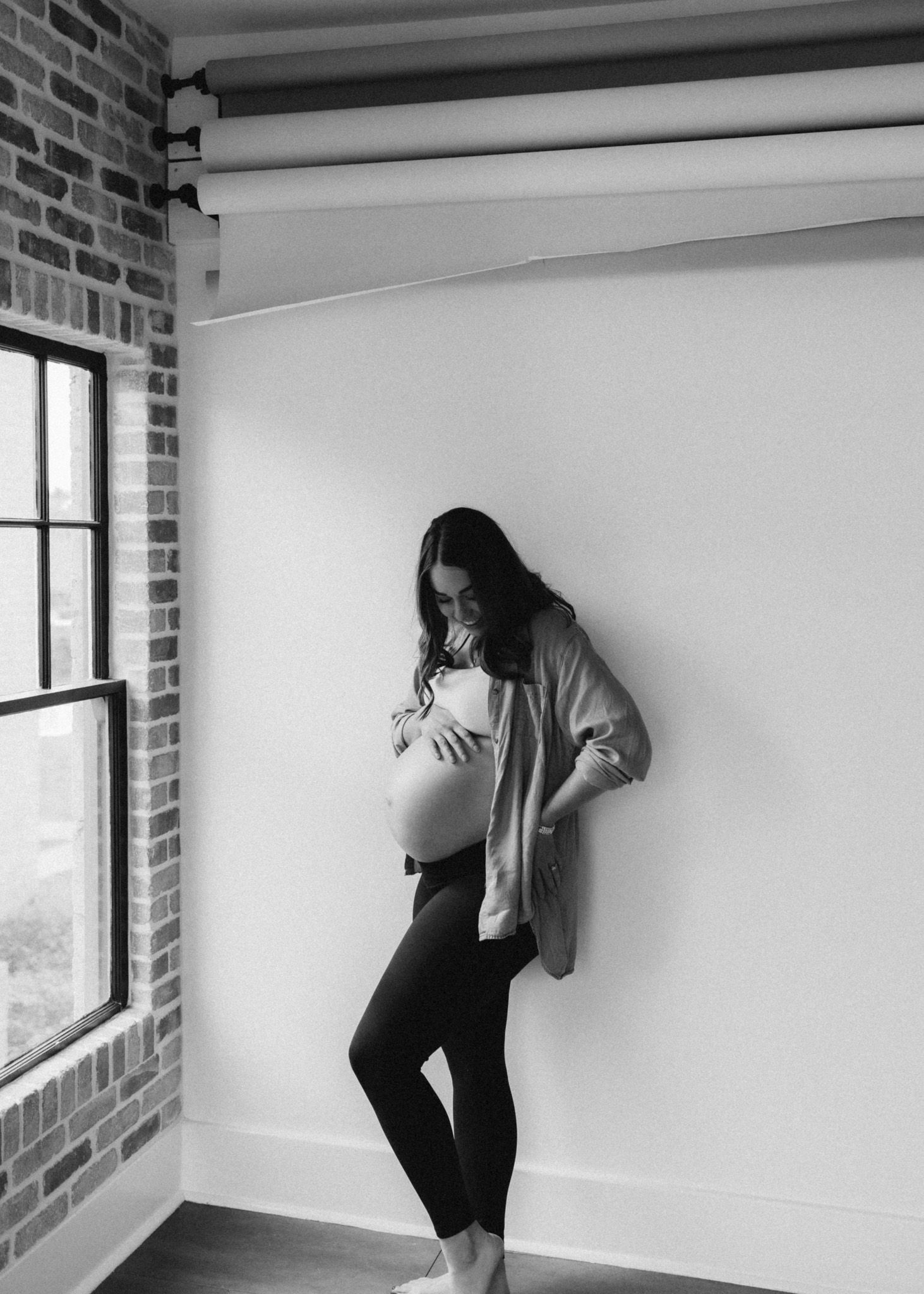 Silhouette of pregnant woman in casual wear standing by window in industrial space.