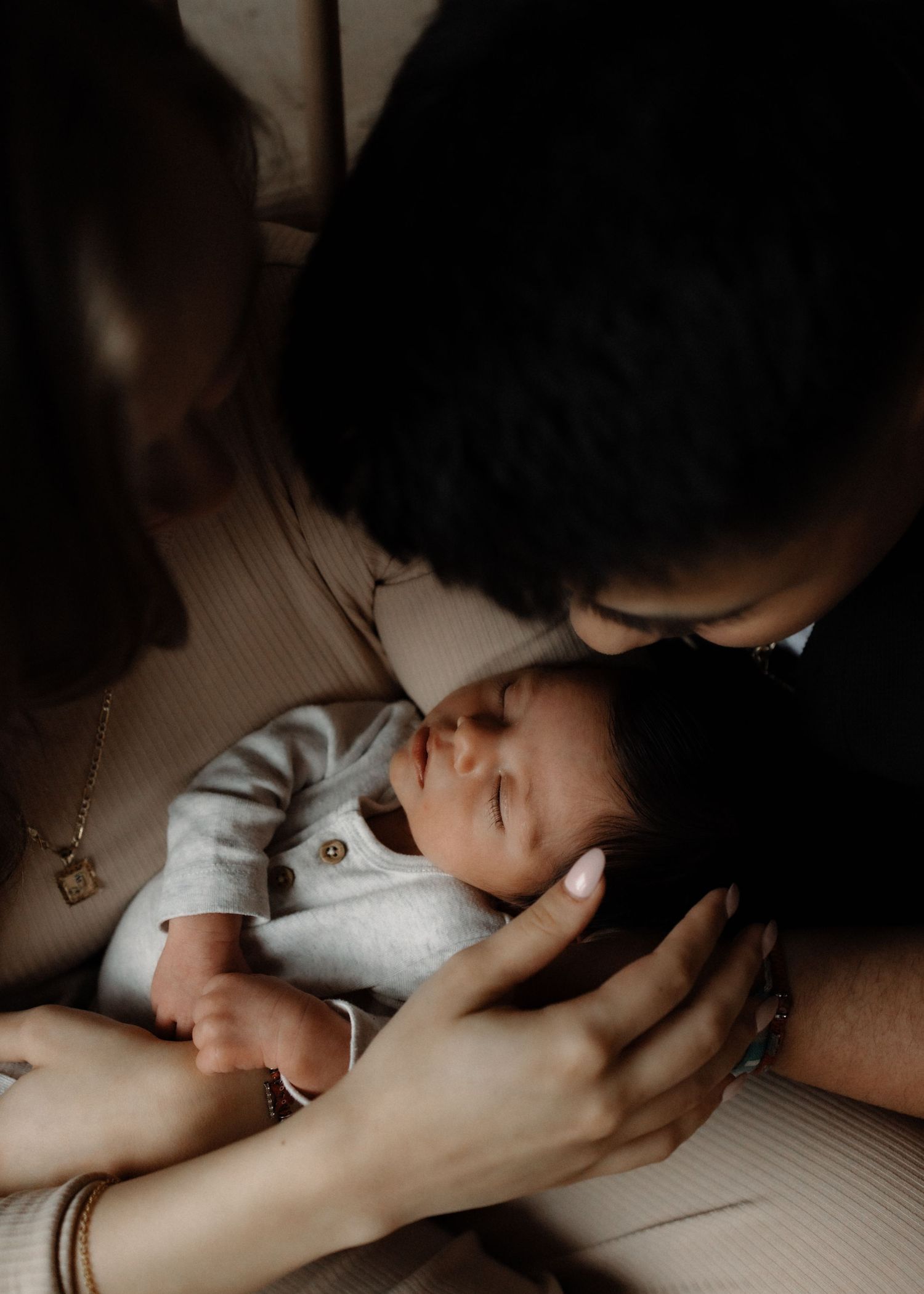 Gentle moment with sleeping infant in white onesie against soft lighting.