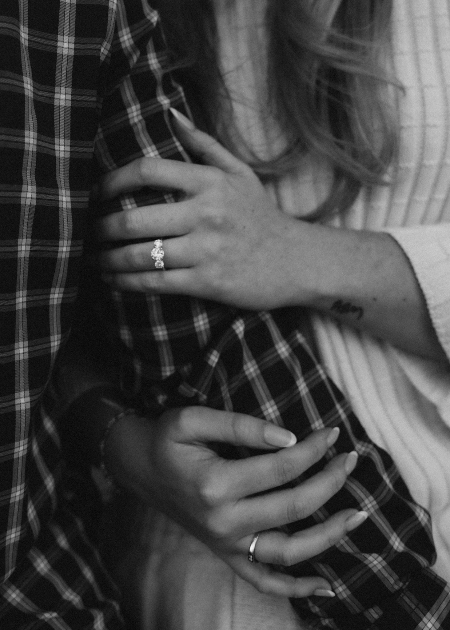 Close-up black and white photo of hands embracing with a diamond ring visible.