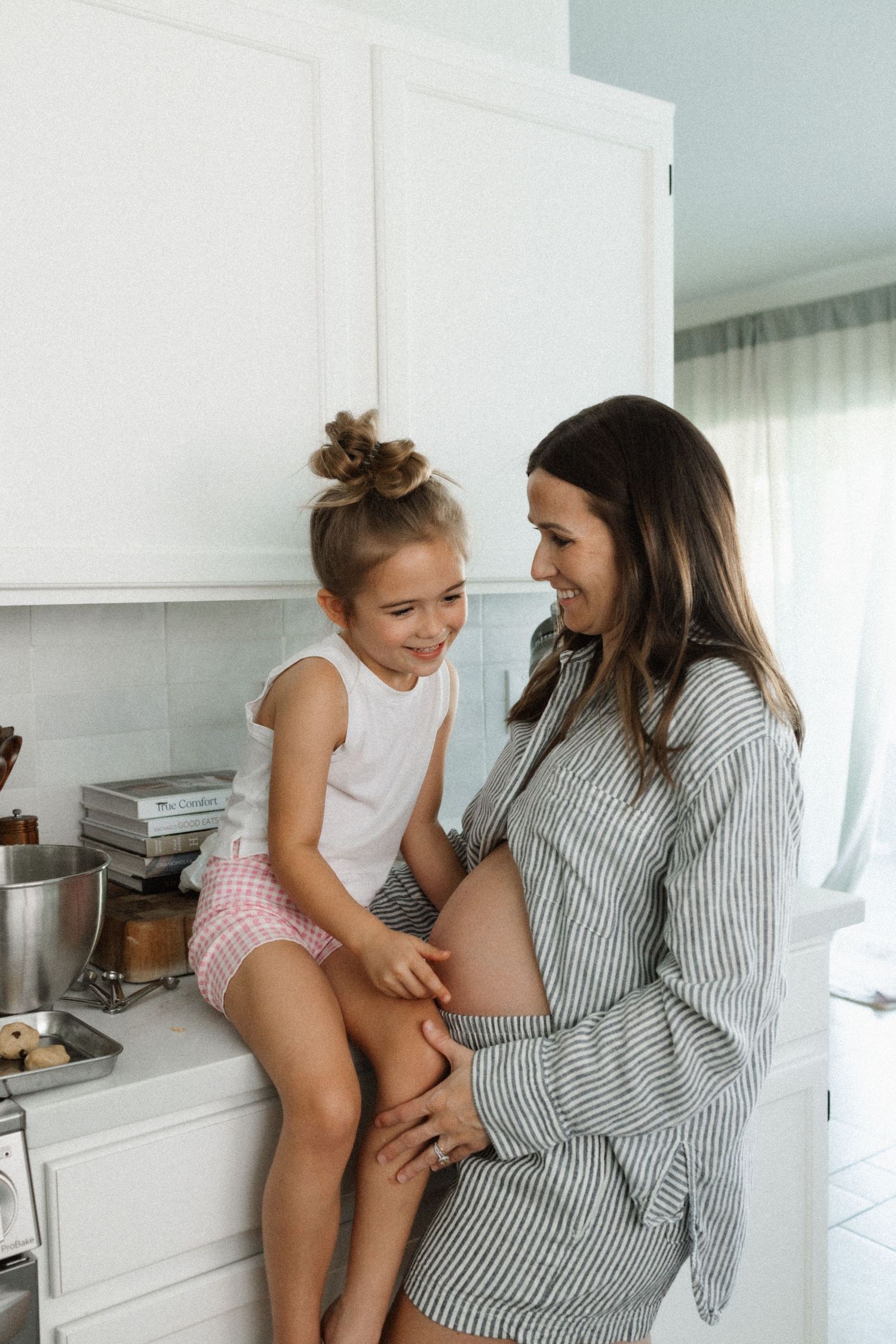 Two people share an intimate conversation while sitting in a bright white modern kitchen.
