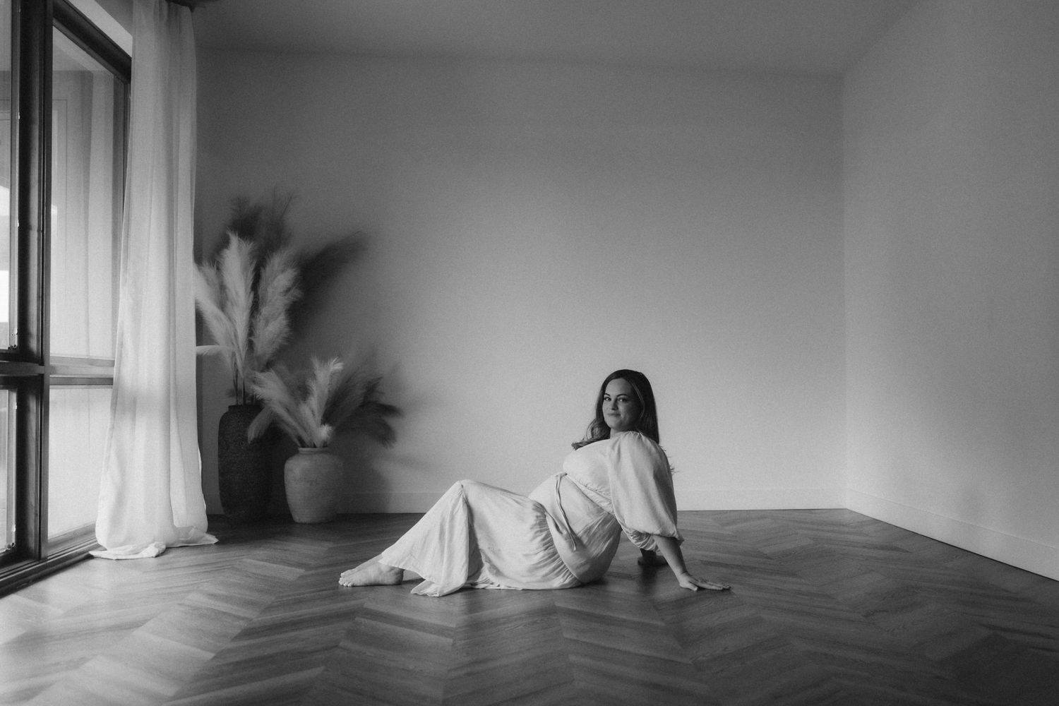 Black and white photo of a person sitting on the floor in a minimalist room with a plant by the window.