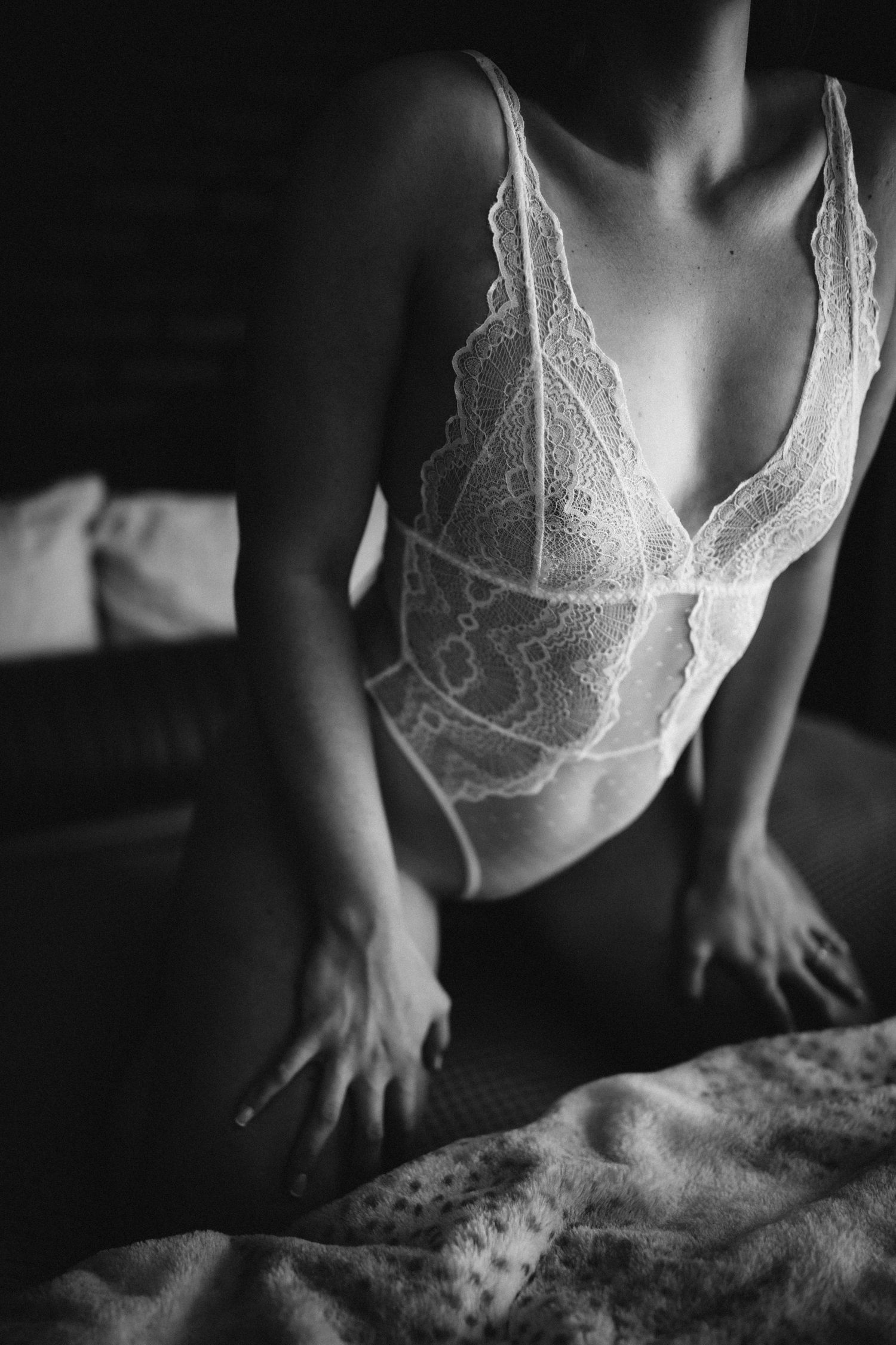 Artistic black and white photo of figure in delicate lace bodysuit on bed.