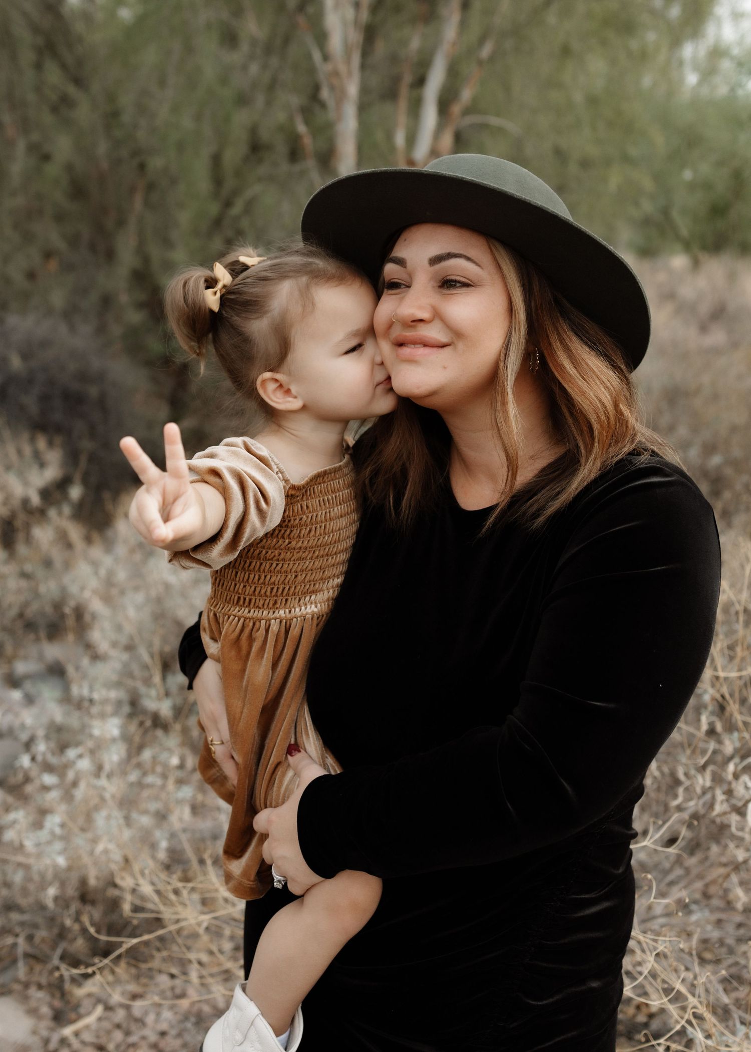Tender moment captured between parent and child wearing matching brown tones in a desert landscape.