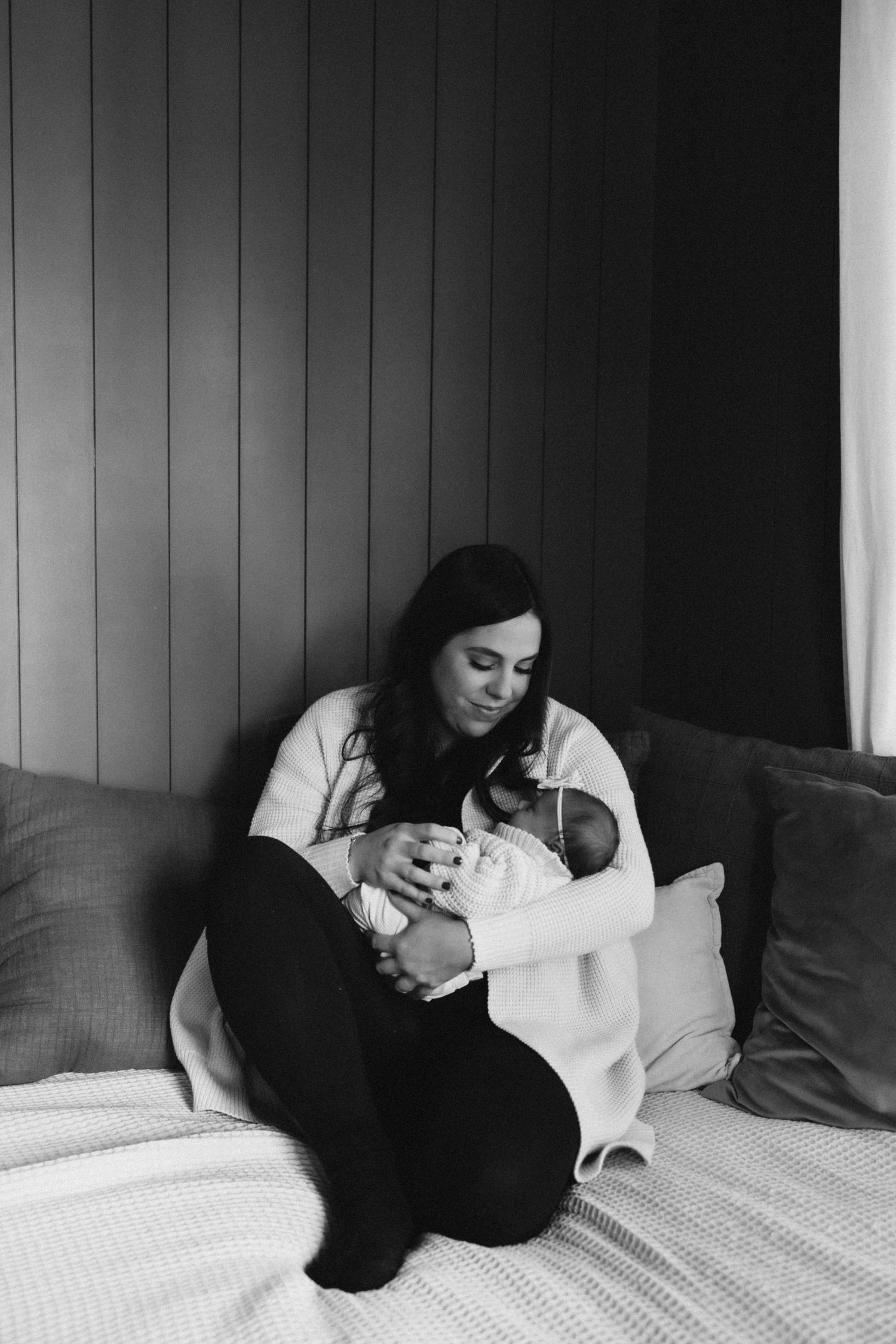 A tender moment captured in black and white as a parent cuddles with newborn baby on a cozy couch.