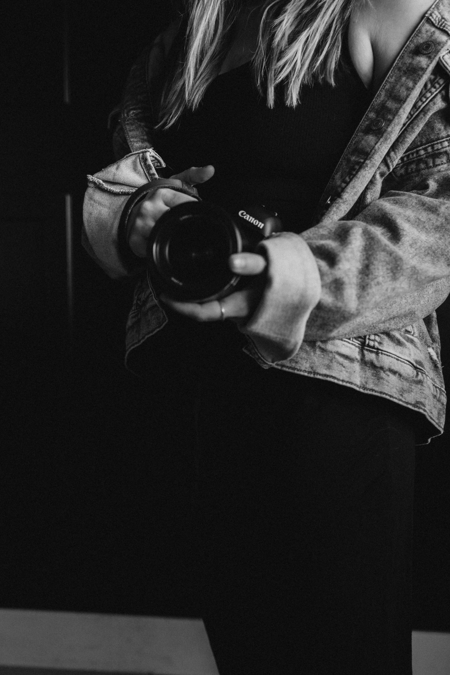 Black and white photo of hands holding a digital camera with a lens against a dark background.