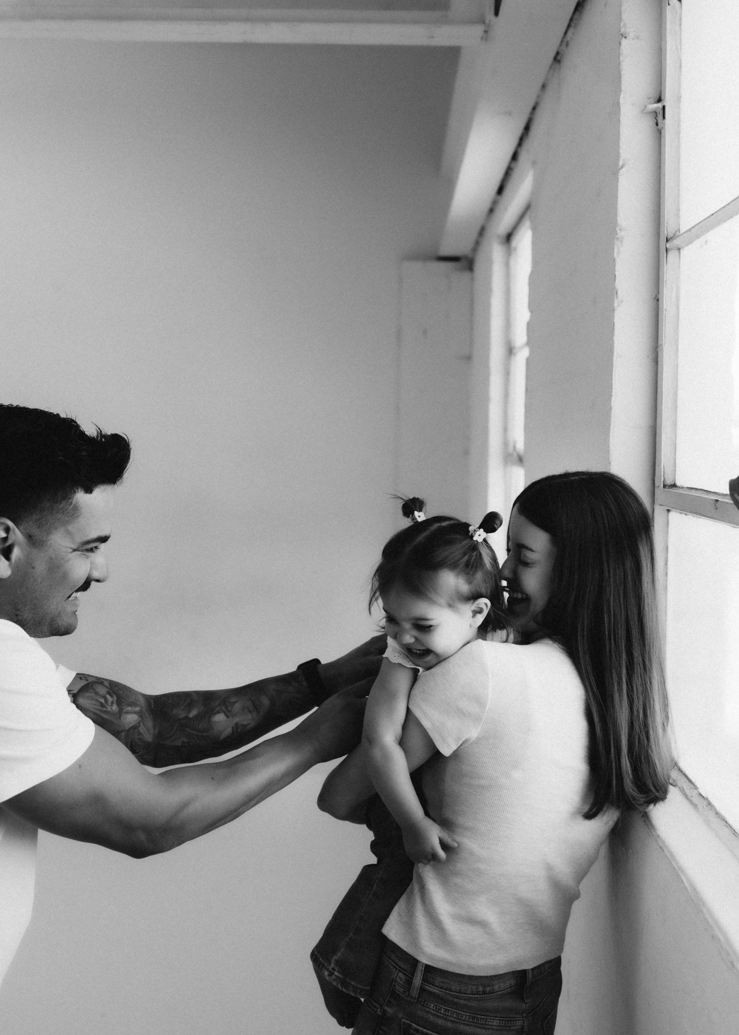 Family sharing playful moment together by window in minimal white space.