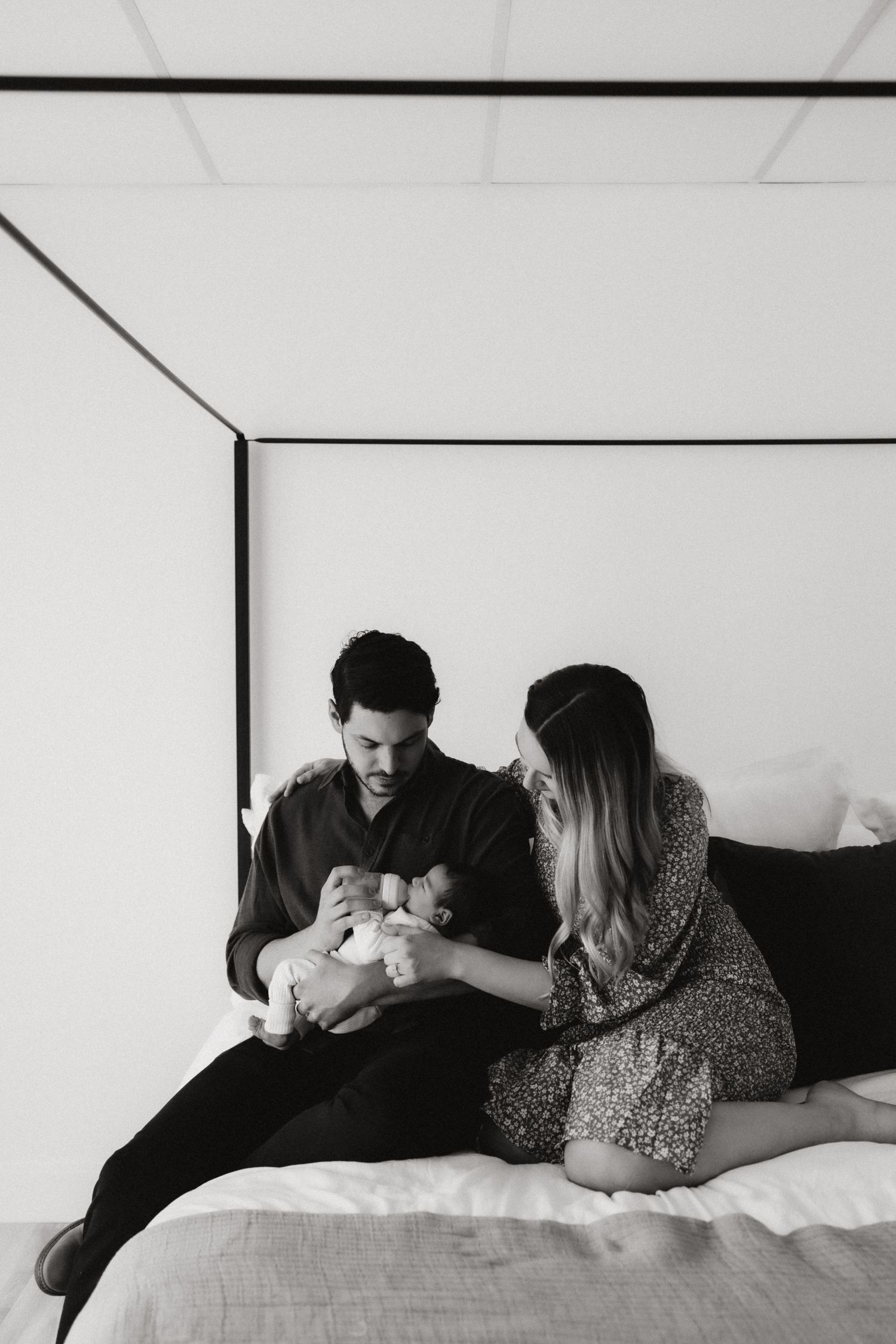 Intimate black and white photo of couple welcoming new baby on bed.