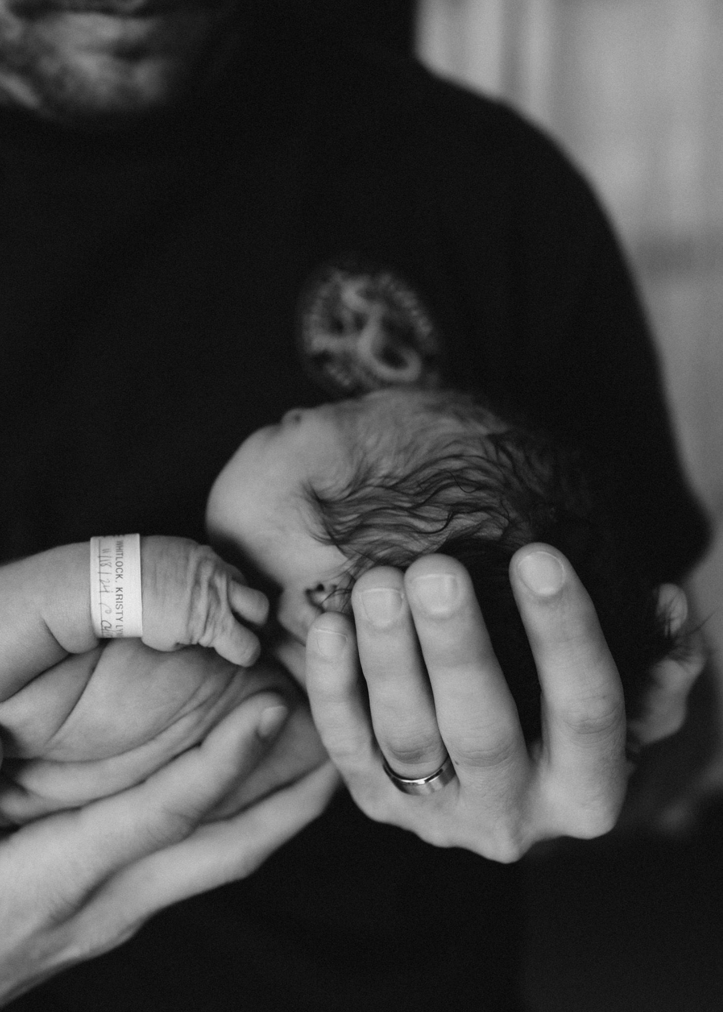 A tender moment showing gentle hands holding a newborn baby with hospital ID bracelet.